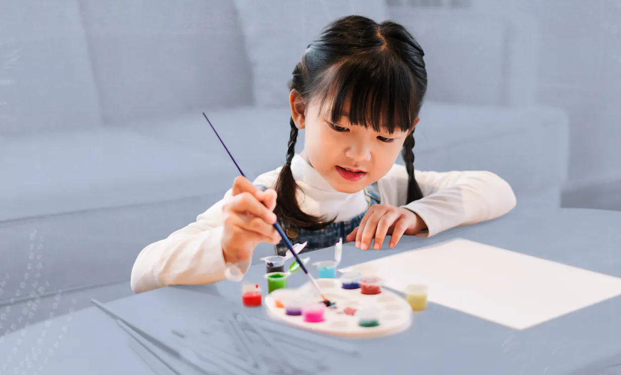A small child sits at a coffee table painting on a piece of paper.