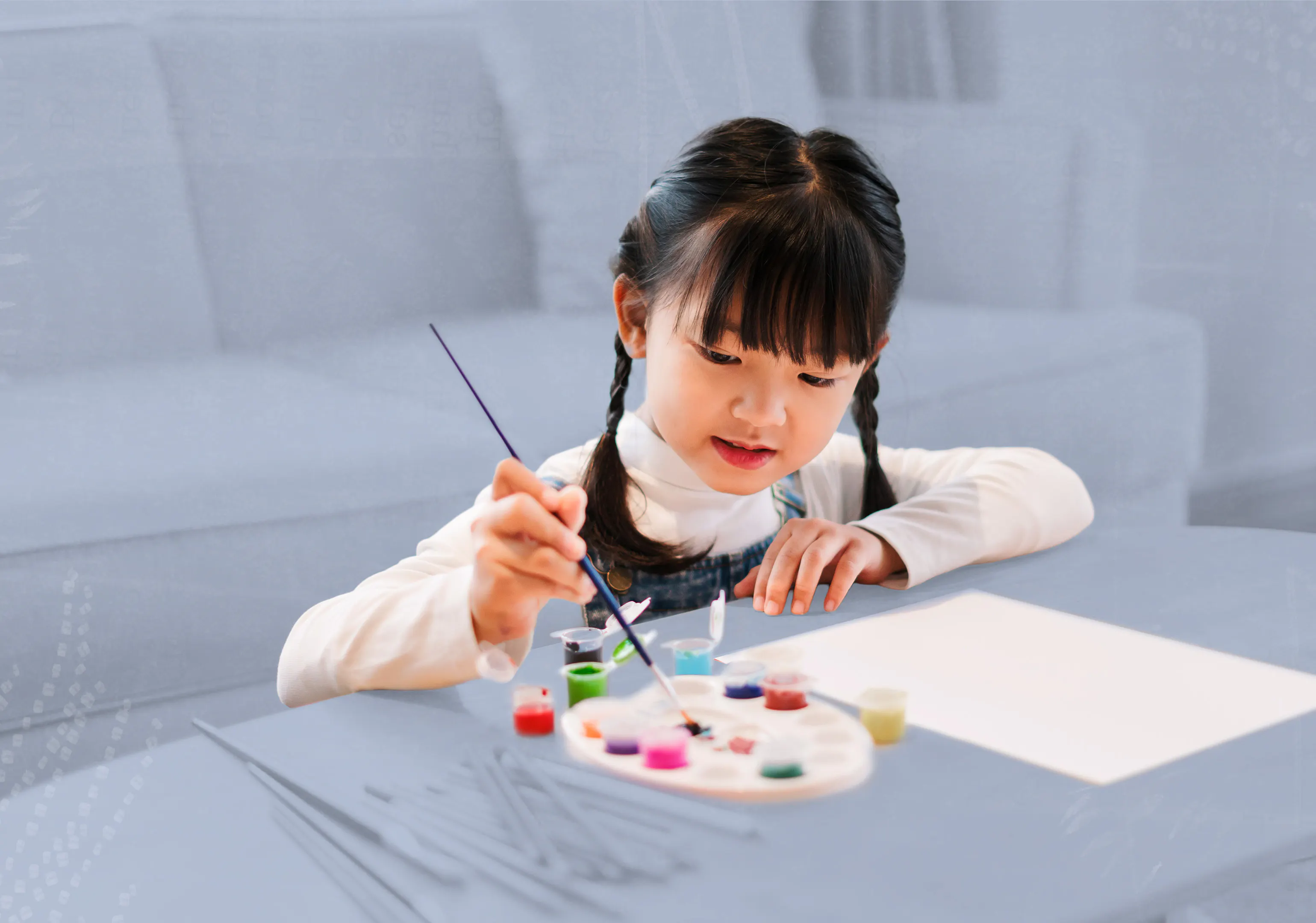 A small child sits at a coffee table painting on a piece of paper.