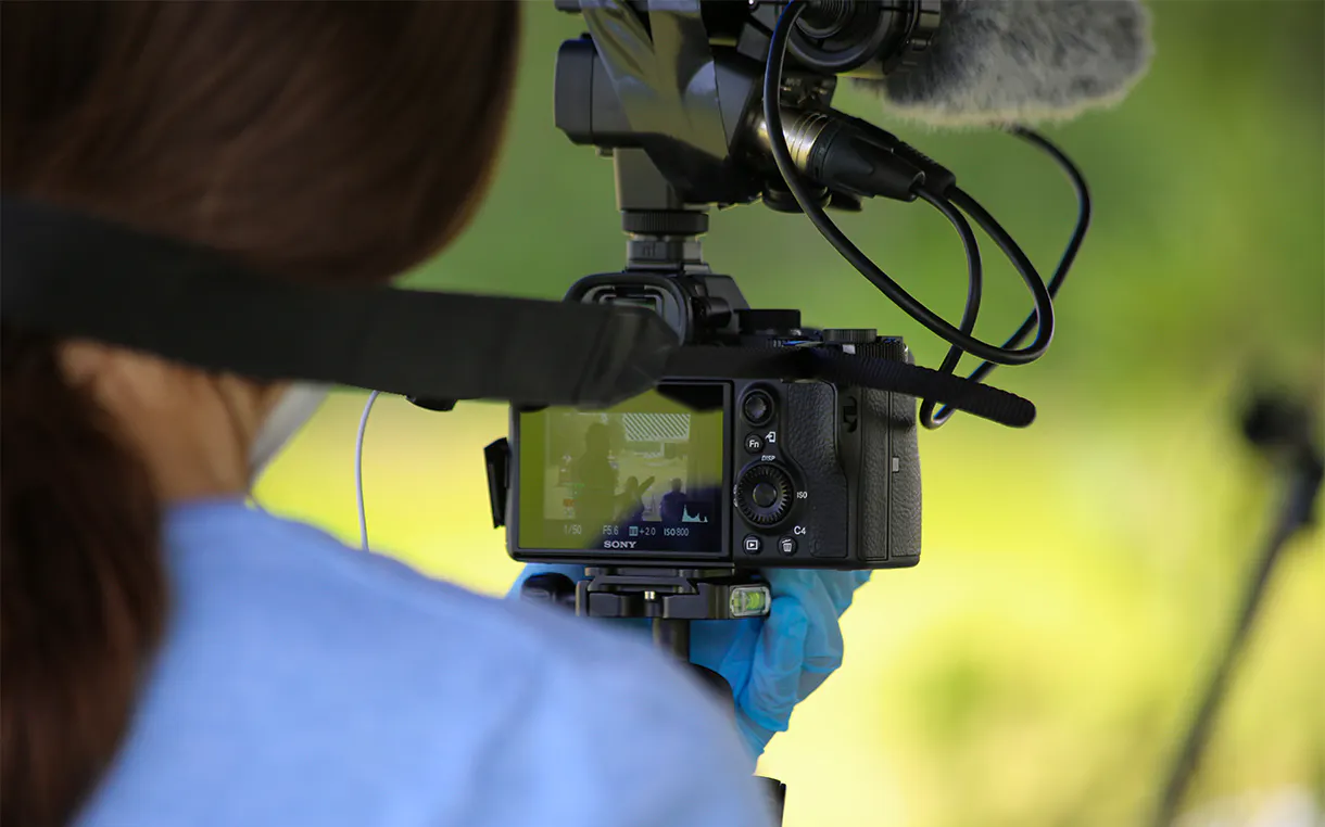 A close up view of the back of a woman's head. The woman is holding a camera recording a video.