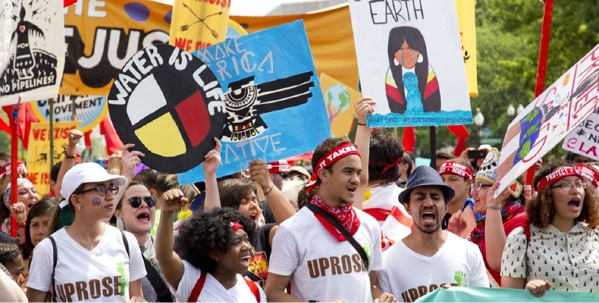 Crowd of people rallying and holding up signs that display messages to fight for climate justice