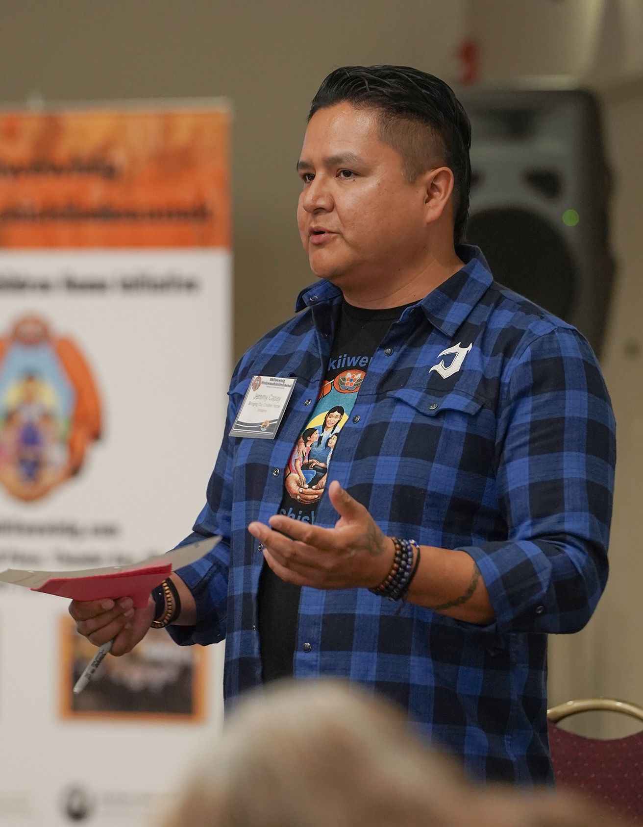Man gestures with his hands while holding papers and a marker