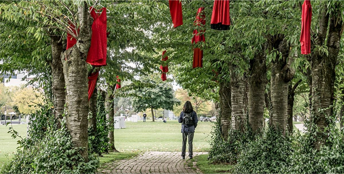 A person walks on a path through trees with red dresses hanging from the branches