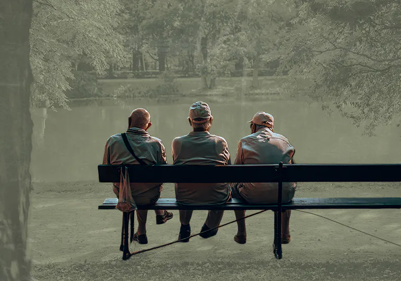 The older men sit on a park bench overlooking a body of water outside.
