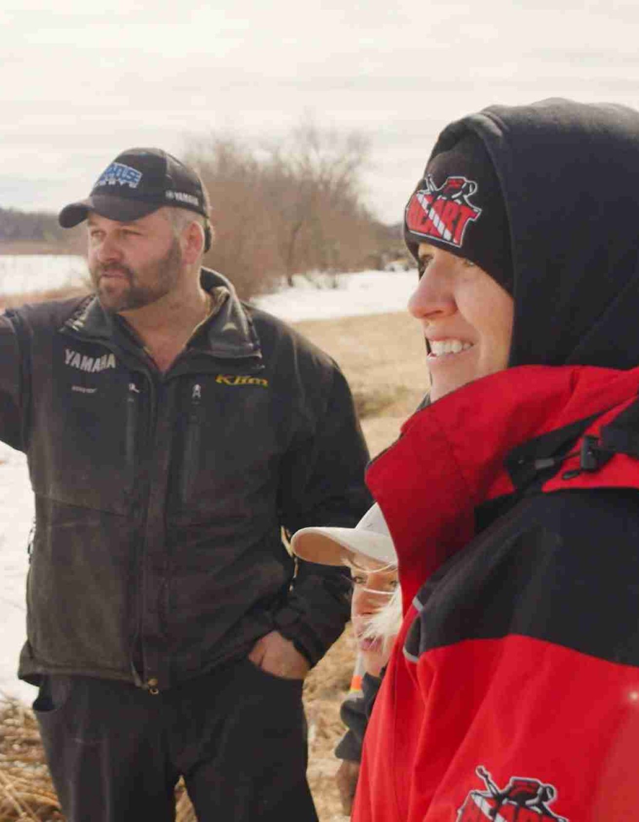 Two individuals in winter gear standing outside looking into the distance