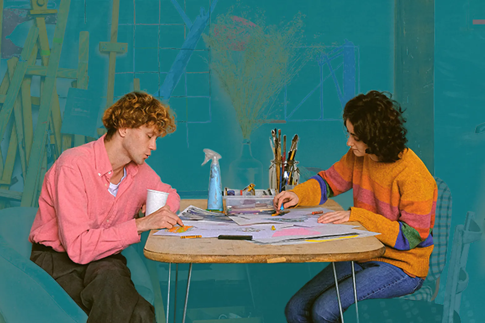 Two people sitting at a table drawing on paper with art supplies behind them.