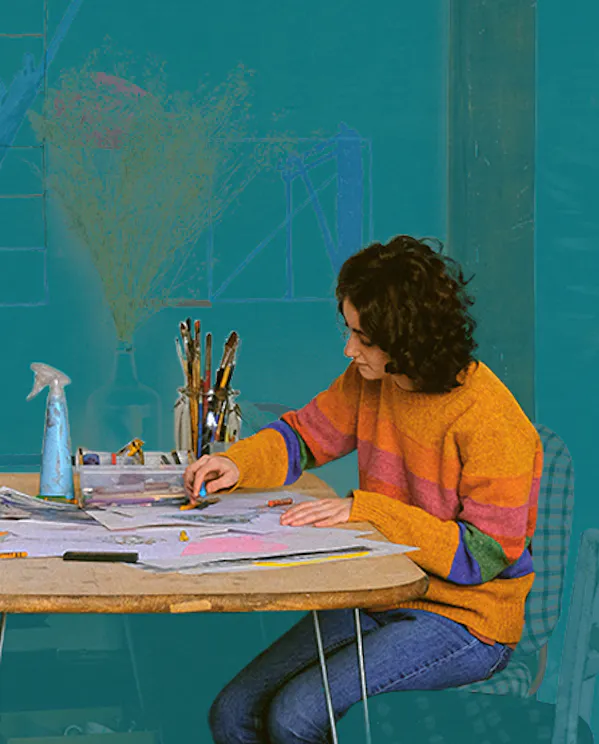 Two people sitting at a table drawing on paper with art supplies behind them.