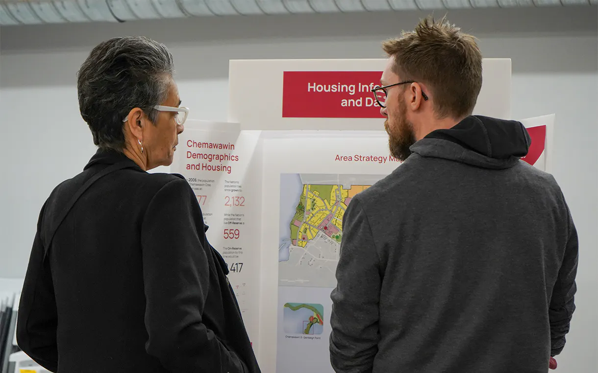 Two people stand in front of an information board talking during a community engagement
