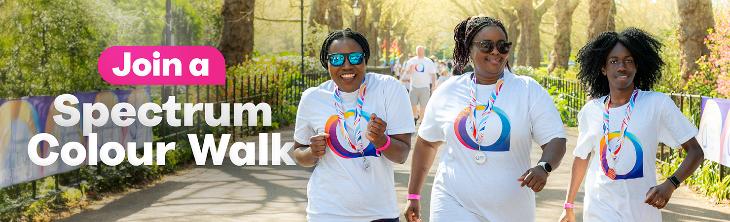 Three people smile as they run along a sunny, tree-lined path, all wearing medals and matching t-shirts. Text overlay reads, 'Join a Spectrum Colour Walk'