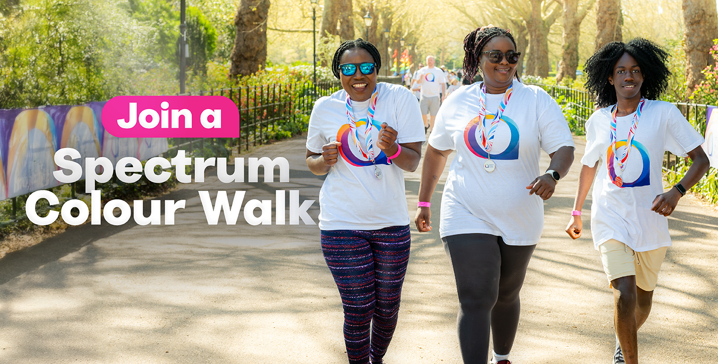 Three people smile as they run along a sunny, tree-lined path, all wearing medals and matching t-shirts. Text overlay reads, 'Join a Spectrum Colour Walk'