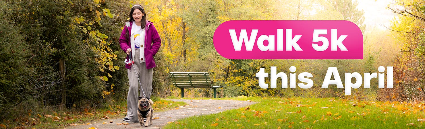 A person walks a small pug on a lead along a path in an autumnal park. A text overlay reads, 'Walk 5k this April'