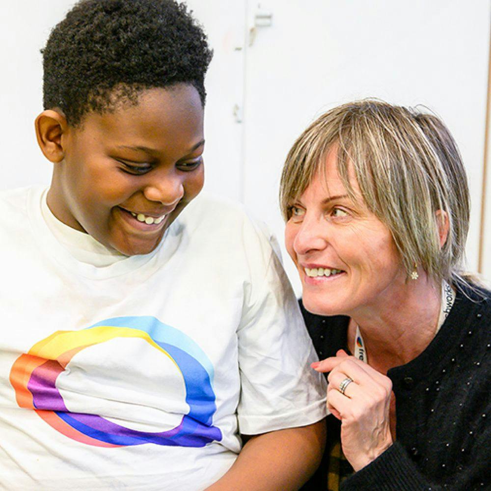 A young student and an adult smile warmly at each other in a classroom setting.