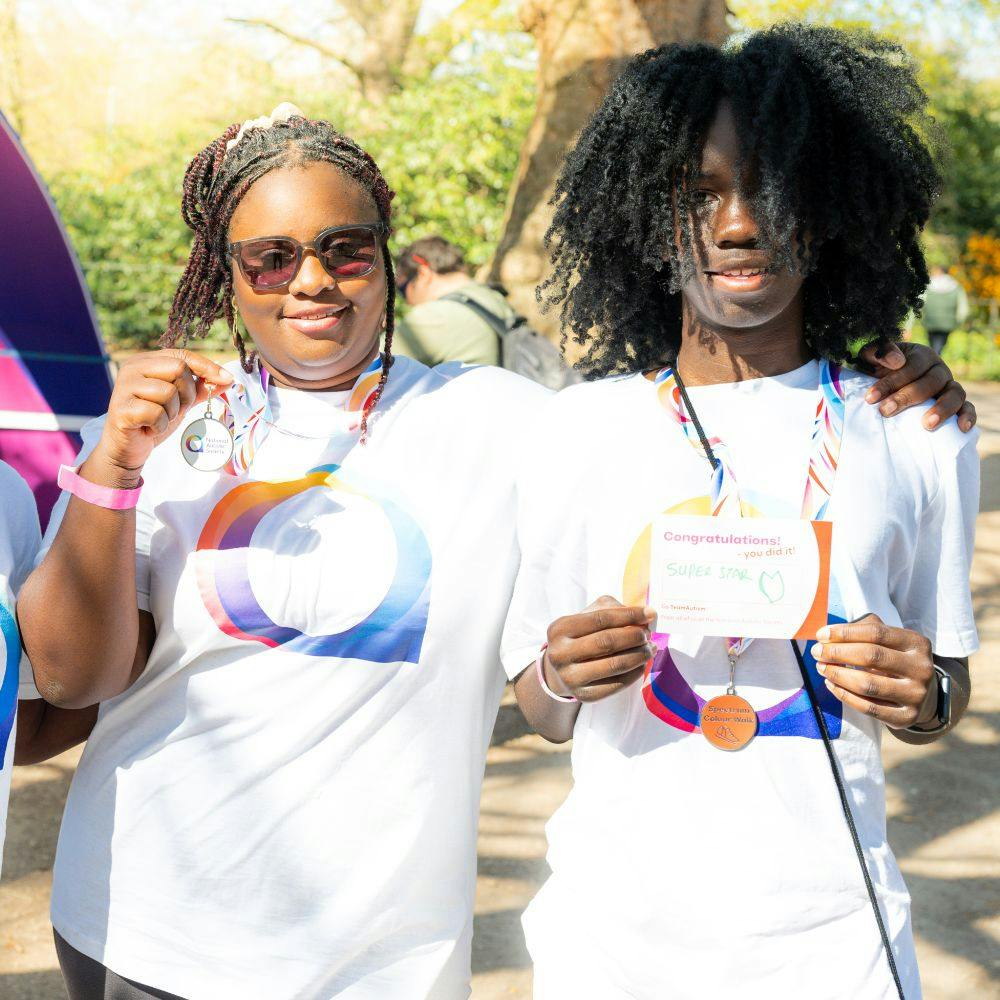 Two people in matching logo t-shirts and medals pose outdoors; one holds a 'Super Star' certificate.