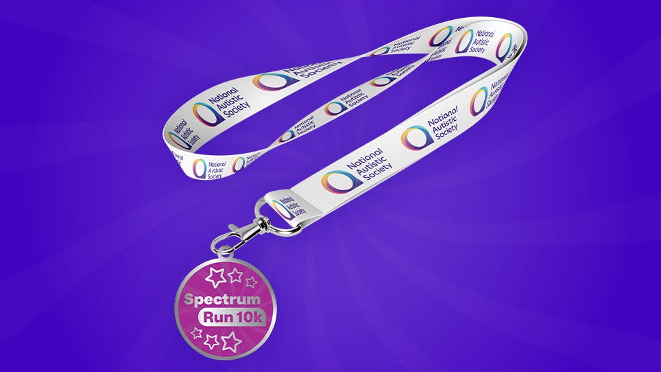Pink “Spectrum Run 10k” medal with star designs attached to a white lanyard featuring the National Autistic Society logo, displayed on a bright purple background.