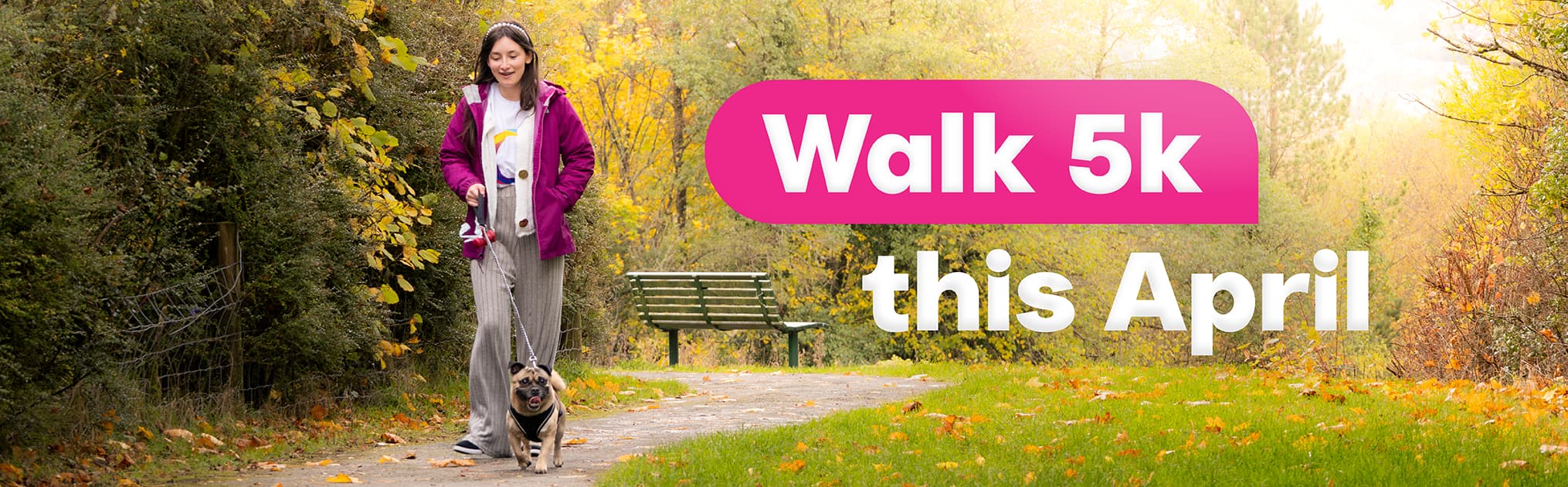 Girl walking one small dog on a leash along a tree-lined park path with fallen leaves and a green bench nearby; bright text reads “Walk 5k this April.”