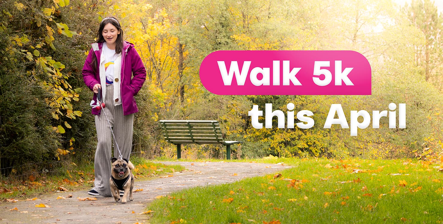 Girl walking one small dog on a leash along a tree-lined park path with fallen leaves and a green bench nearby; bright text reads “Walk 5k this April.”