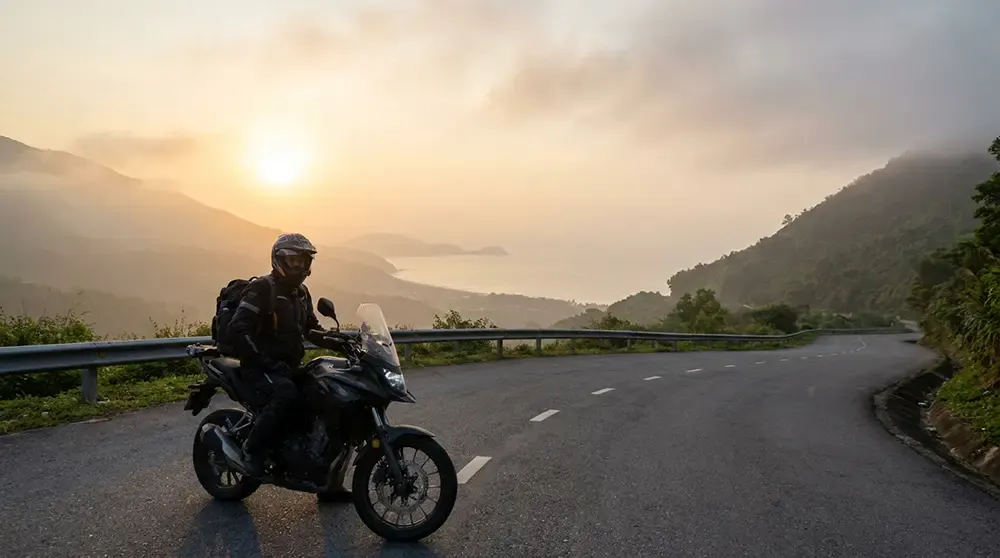 Rider in full gear cresting the Hai Van Pass at sunrise, ocean visible in background