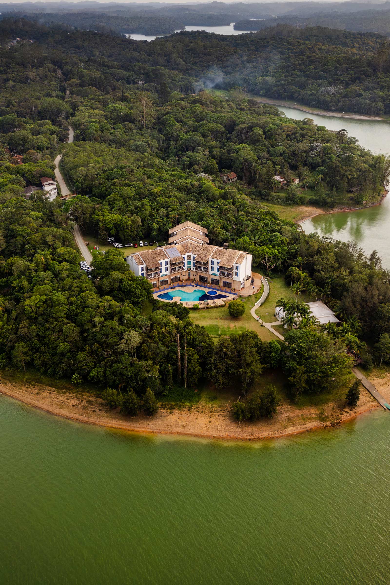 Imagem aérea de resort na represa com grande vegetação ao fundo