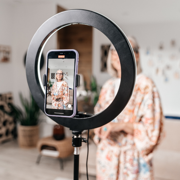 Young woman in front of her smartphone with a ring light. She is recording herself doing a social media video.