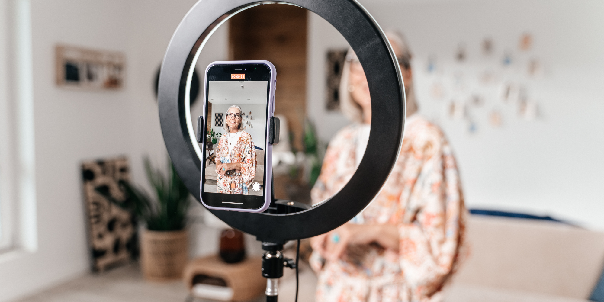 Young woman in front of her smartphone with a ring light. She is recording herself doing a social media video.