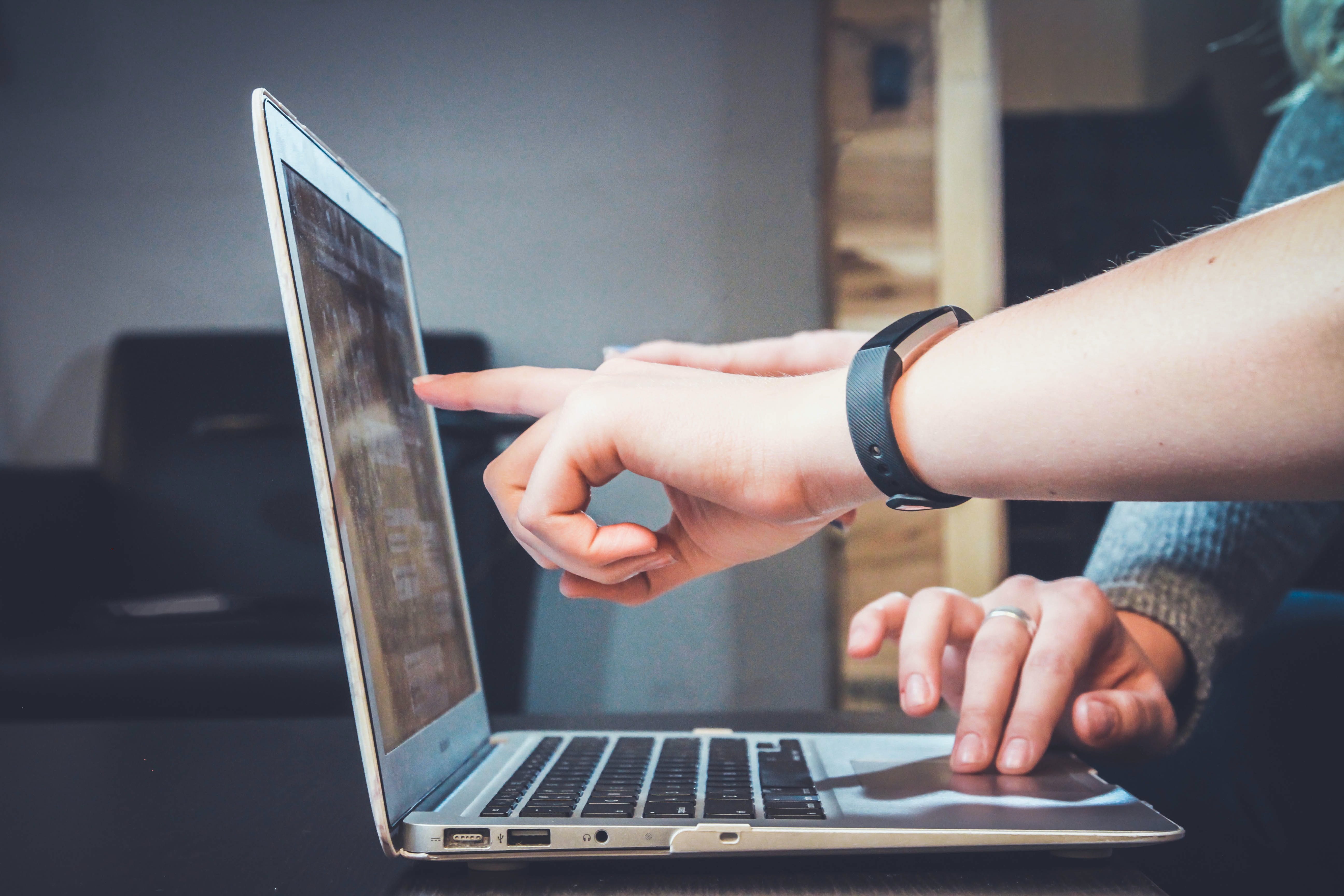 A hand pointing to an open laptop screen