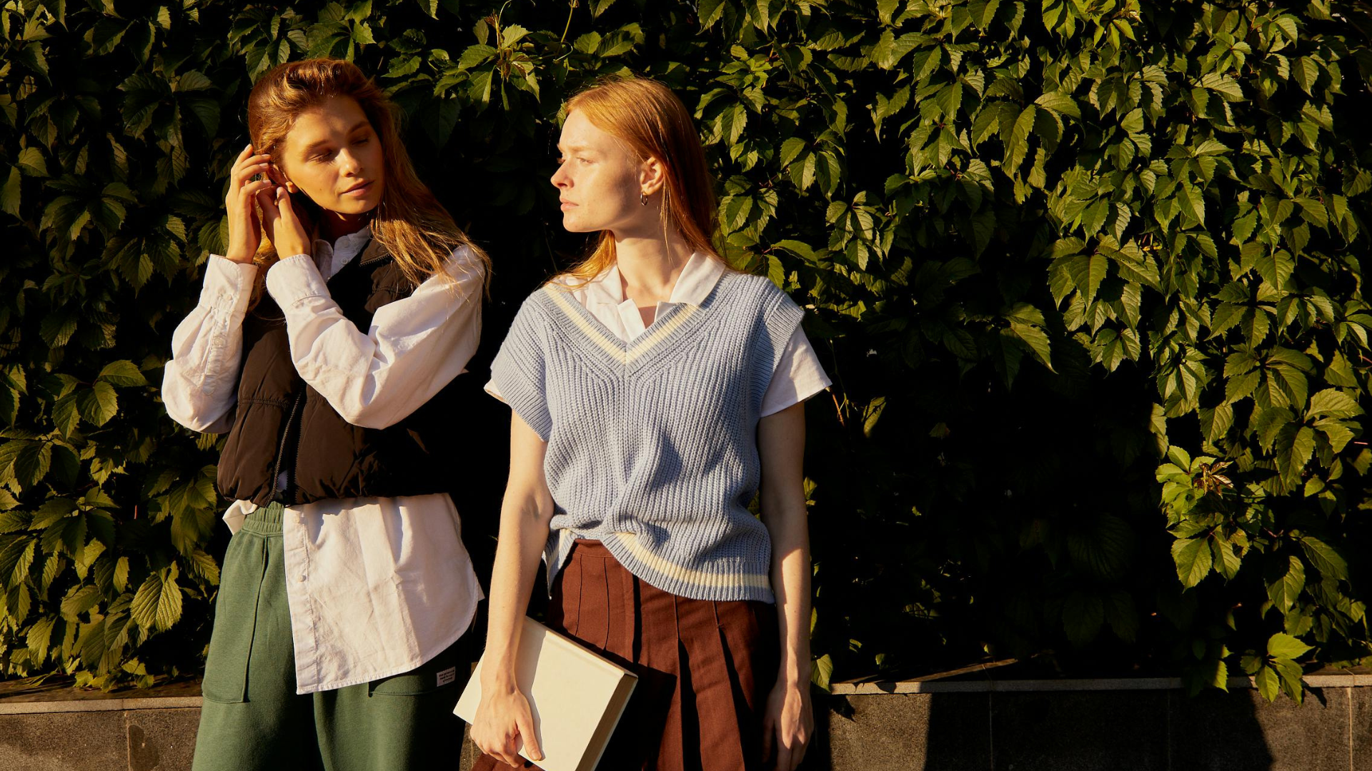 Two smartly dressed students looking at each other, in front of a green shrub.