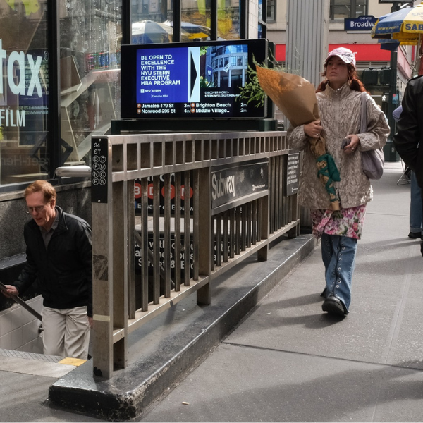 Woman walking by subway with NYU EMBA ad behind her 