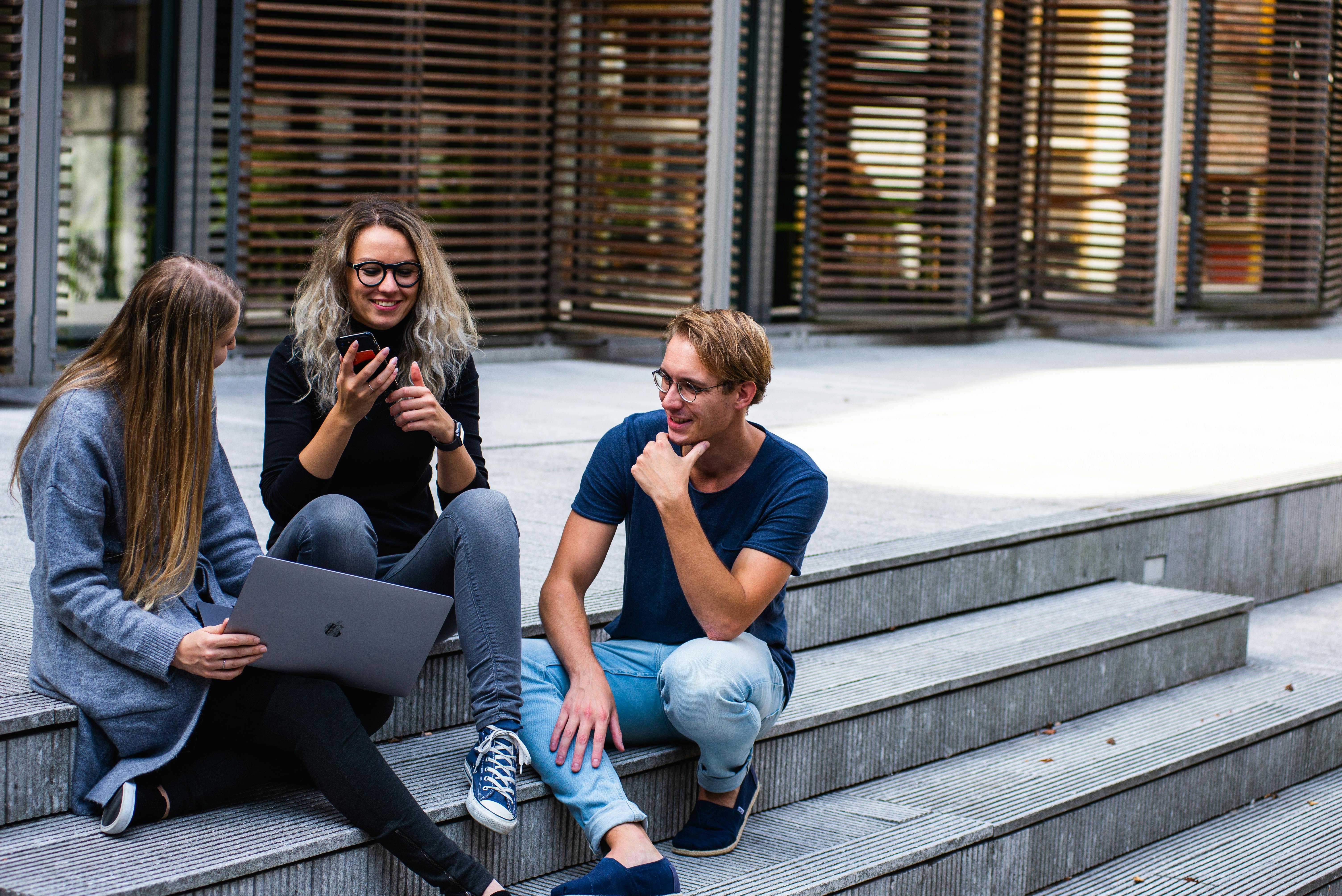 Three students around a laptop smiling together 