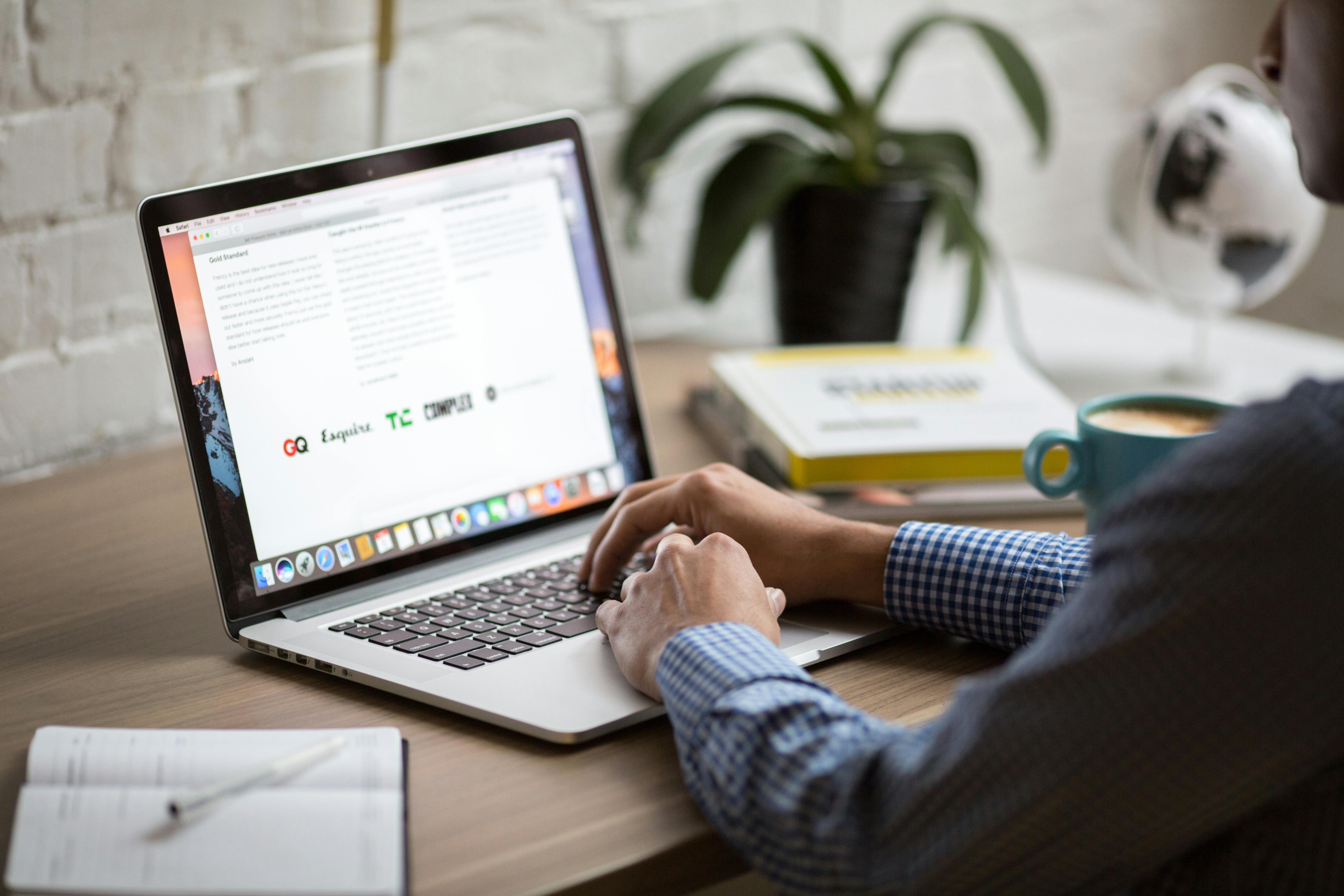 Person typing on laptop with a notepad and plant on the table