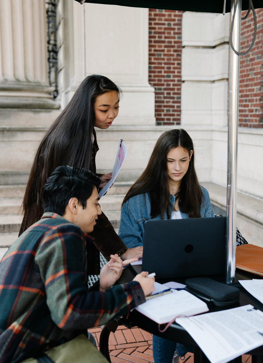 3 students doing work at a table looking at one laptop screen