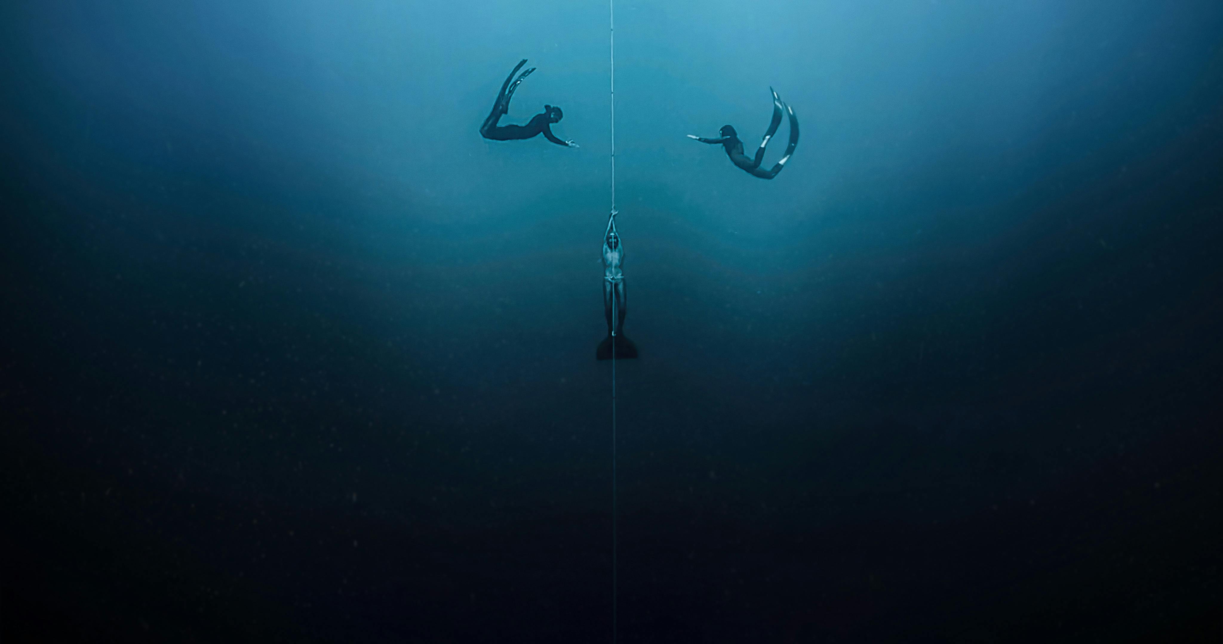 Three divers orient around a diving cable in a dark blue ocean.