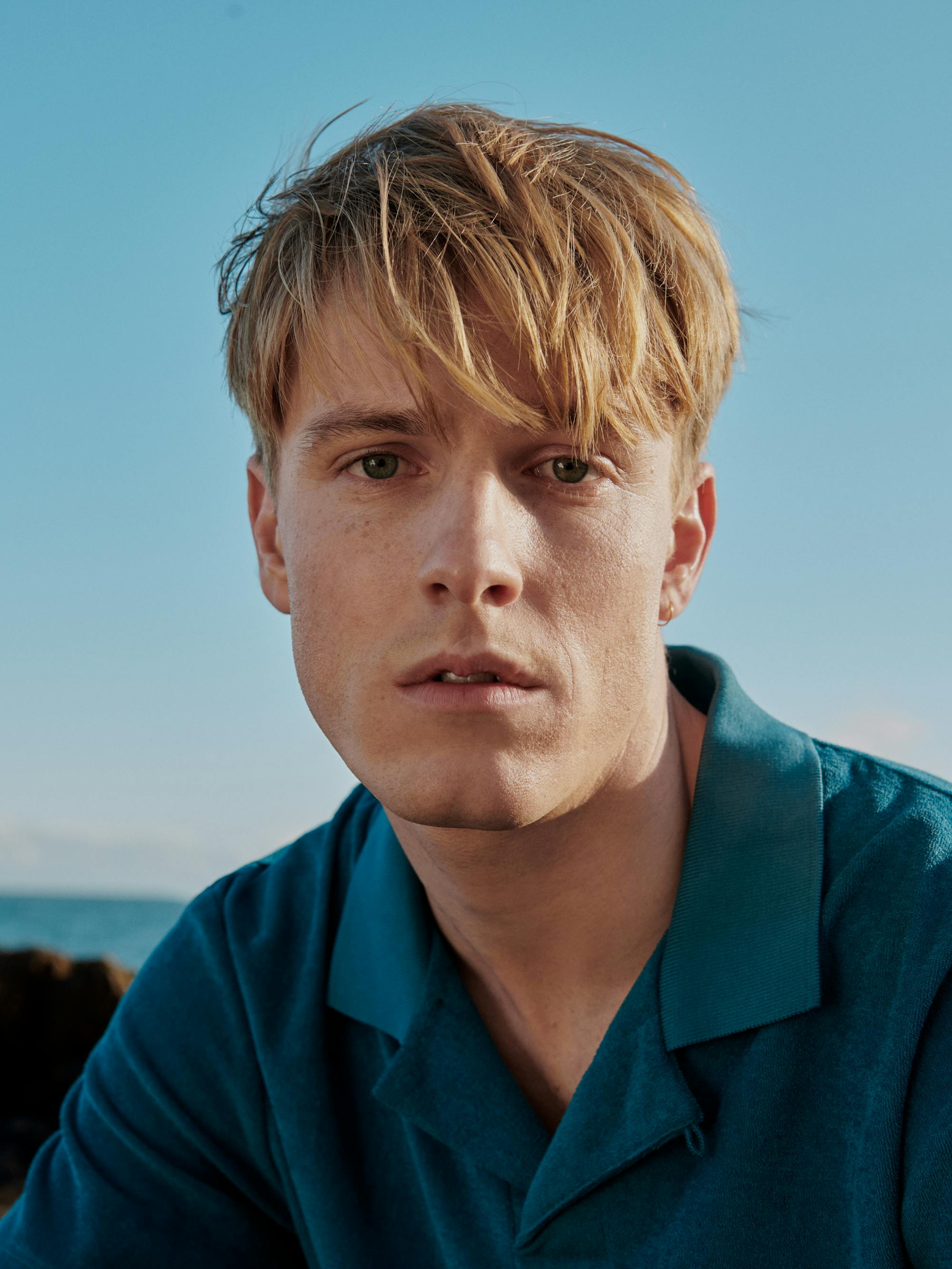 Louis Hofmann wears a teal polo and looks yearningly at the camera.