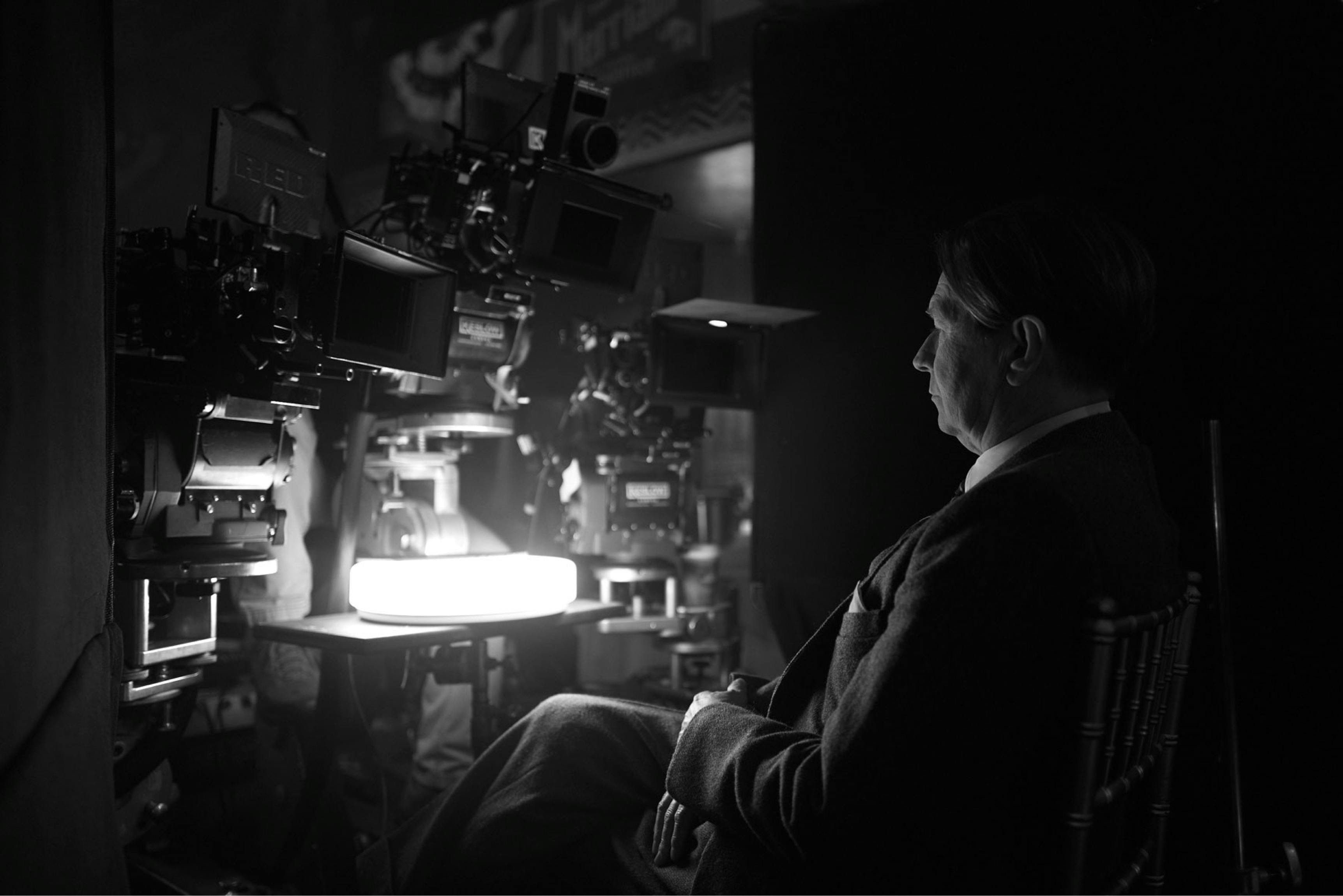 Gary Oldman in costume as Herman J. Mankiewicz sits behind a series of cameras on the set of Mank.