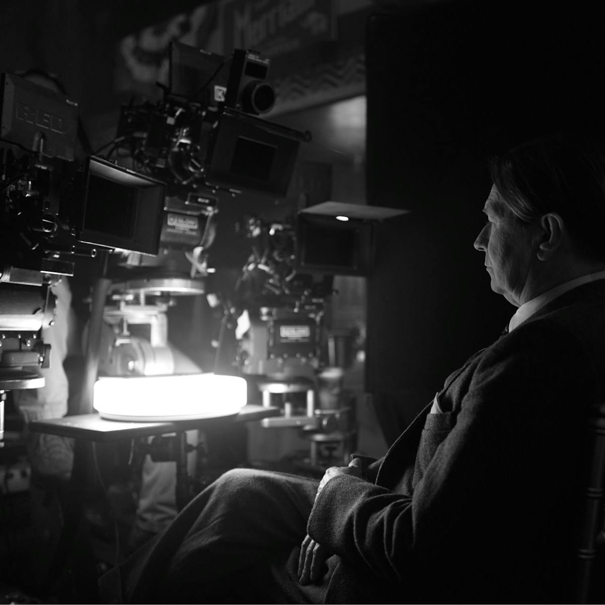 Gary Oldman in costume as Herman J. Mankiewicz sits behind a series of cameras on the set of Mank.
