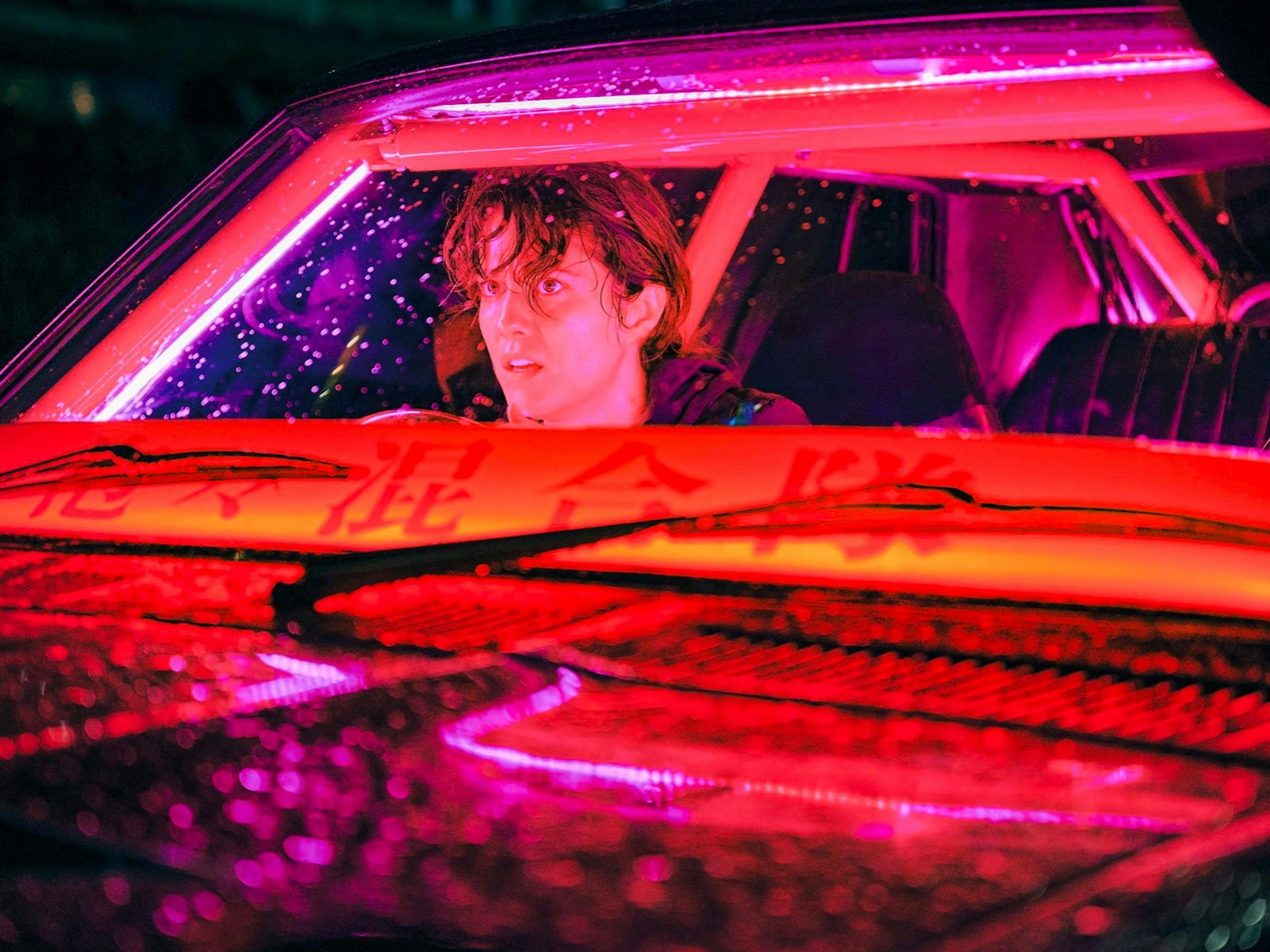 Kate (Mary Elizabeth Winstead) sits in a car lit by pink and orange neon light.