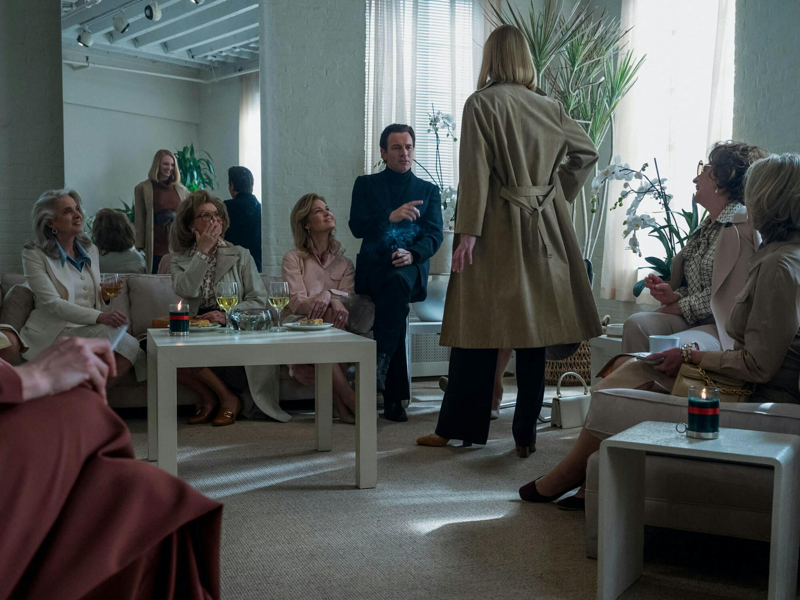 Halston sits with a bevy of older women in a neutral toned room. He stands out in his black ensemble.