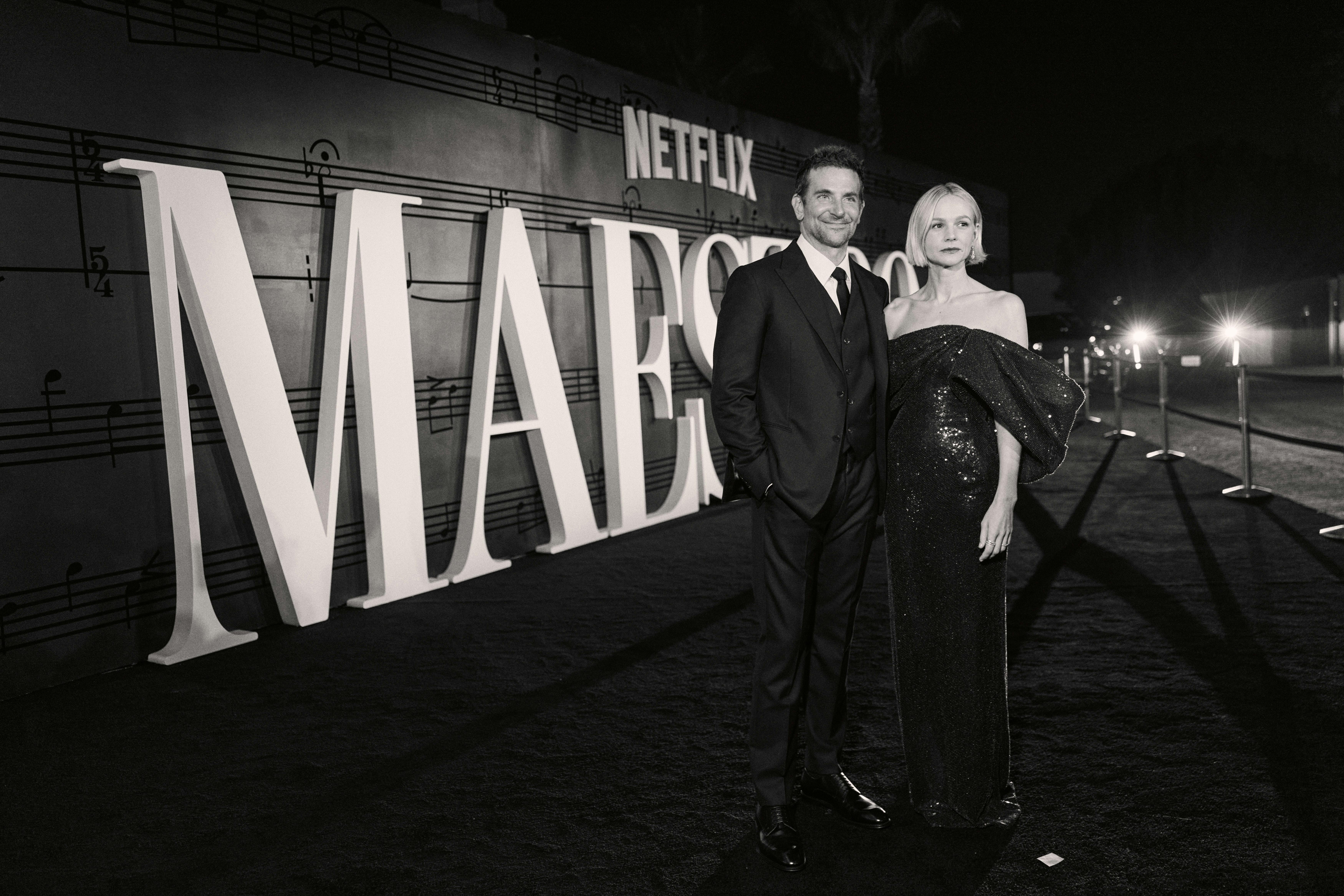 Bradley Cooper and Carey Mulligan stand on a black carpet next to 'MAESTRO' in white letters.