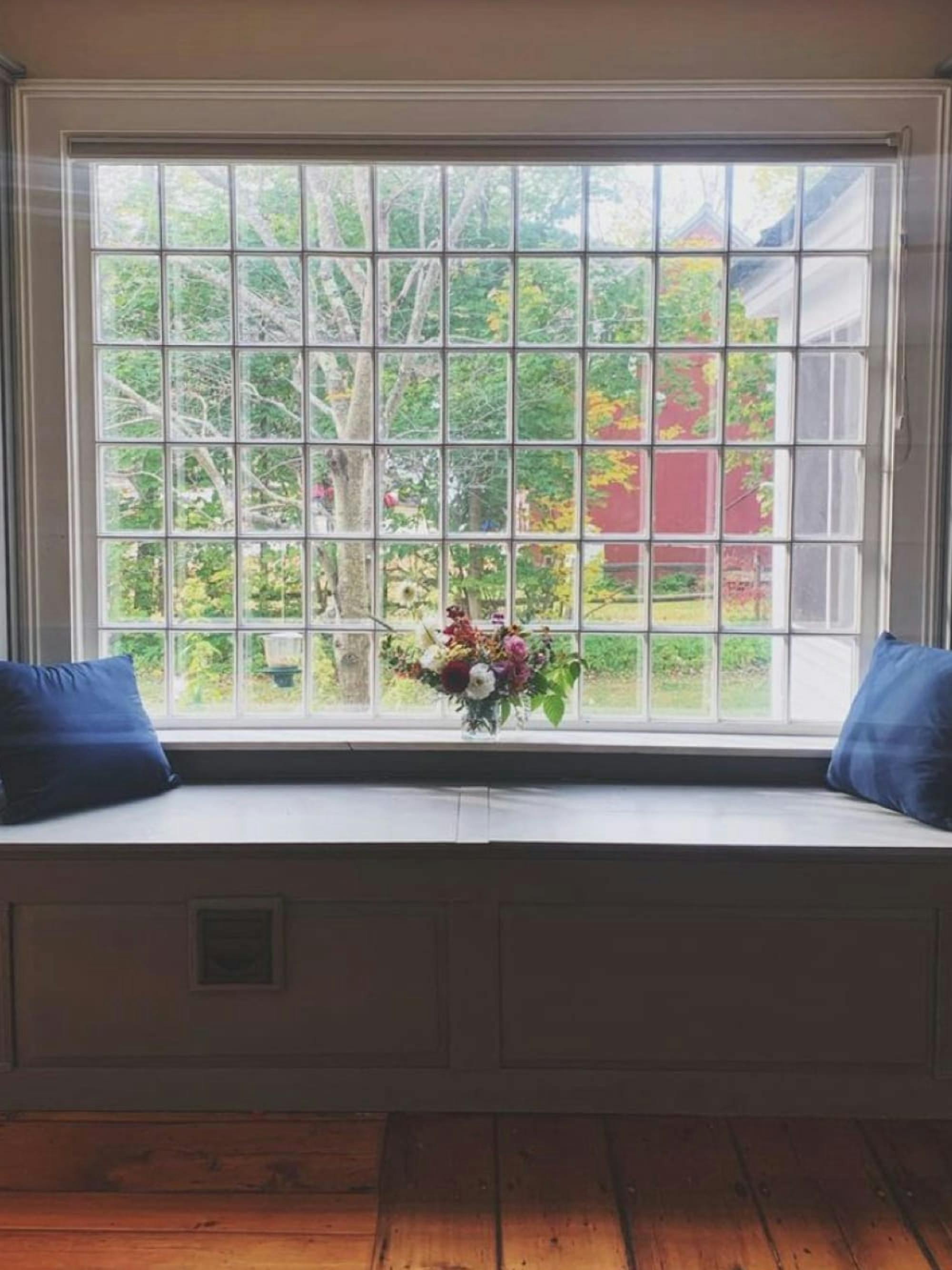 A window seat looking out on fall foliage. The bench is framed by two navy pillows.