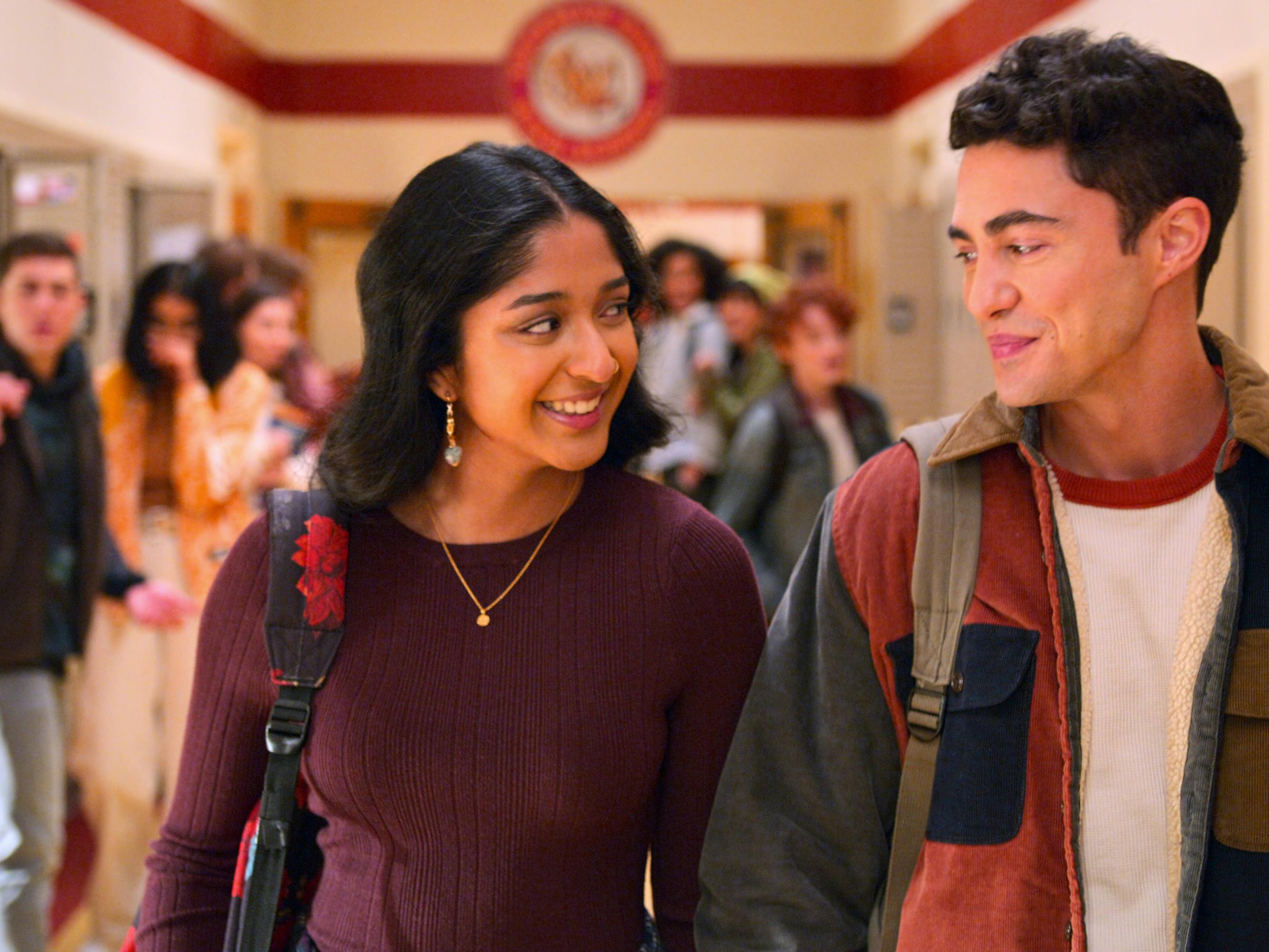 Devi Vishwakumar (Maitreyi Ramakrishnan) and Paxton Hall-Yoshida (Darren Barnet) walk through the school hallways as other students look on shocked.
