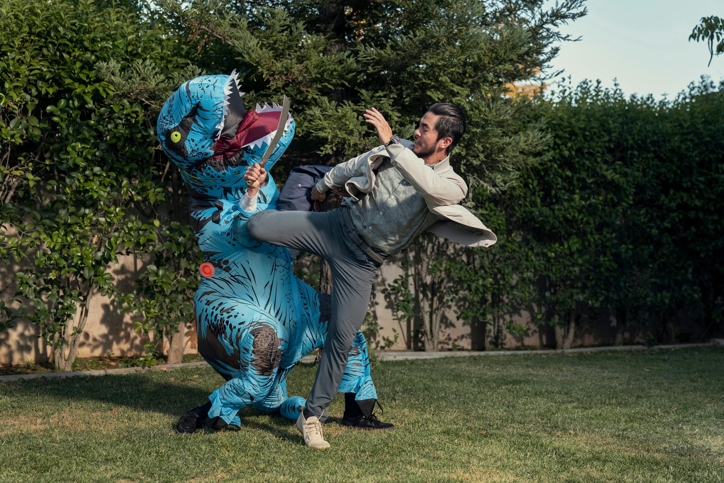 Charles Sun (Justin Chien) kicks someone in a blow-up dinosaur costume in a back yard.
