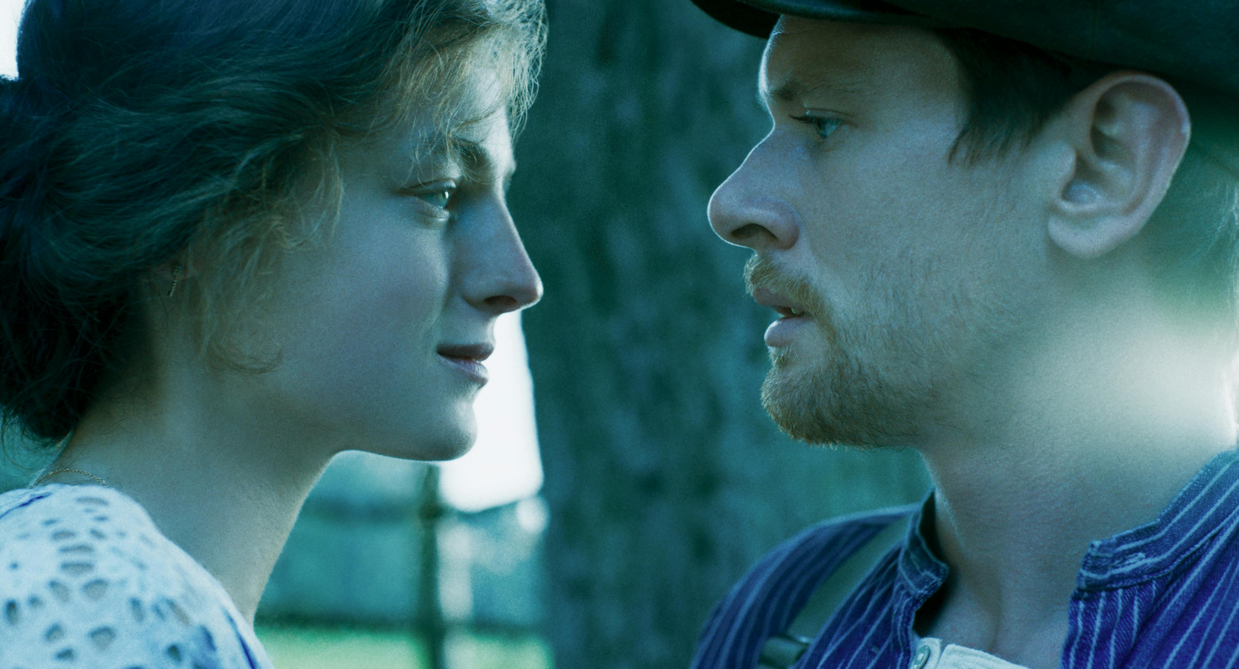 Lady Chatterley (Emma Corrin) and Oliver Mellors (Jack O'Connell) face off in a green hued light.