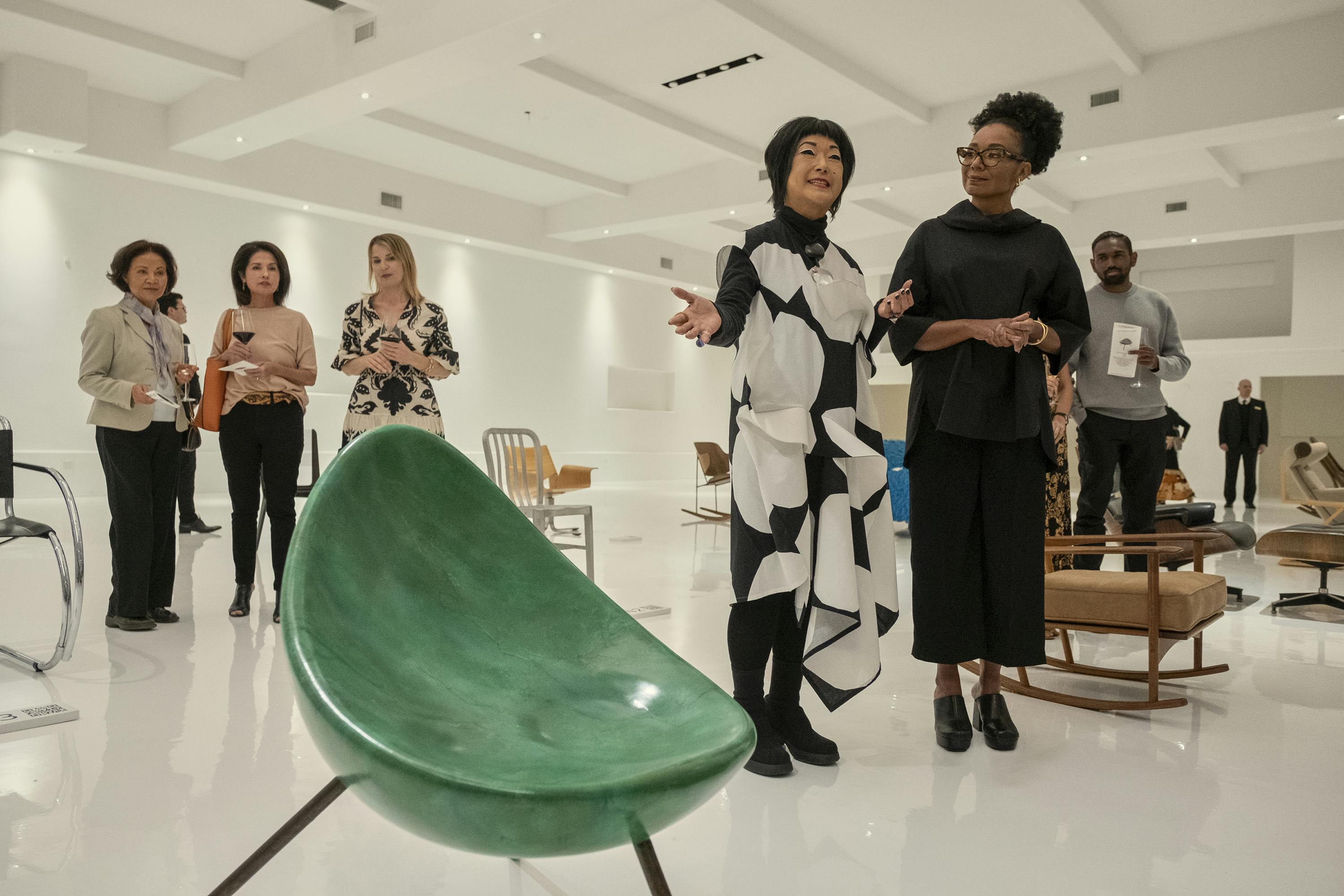 Fumi (Patti Yasutake) talks to a crowd of people about the green Tamago chair, which sits threateningly in the foreground of this shot.  
