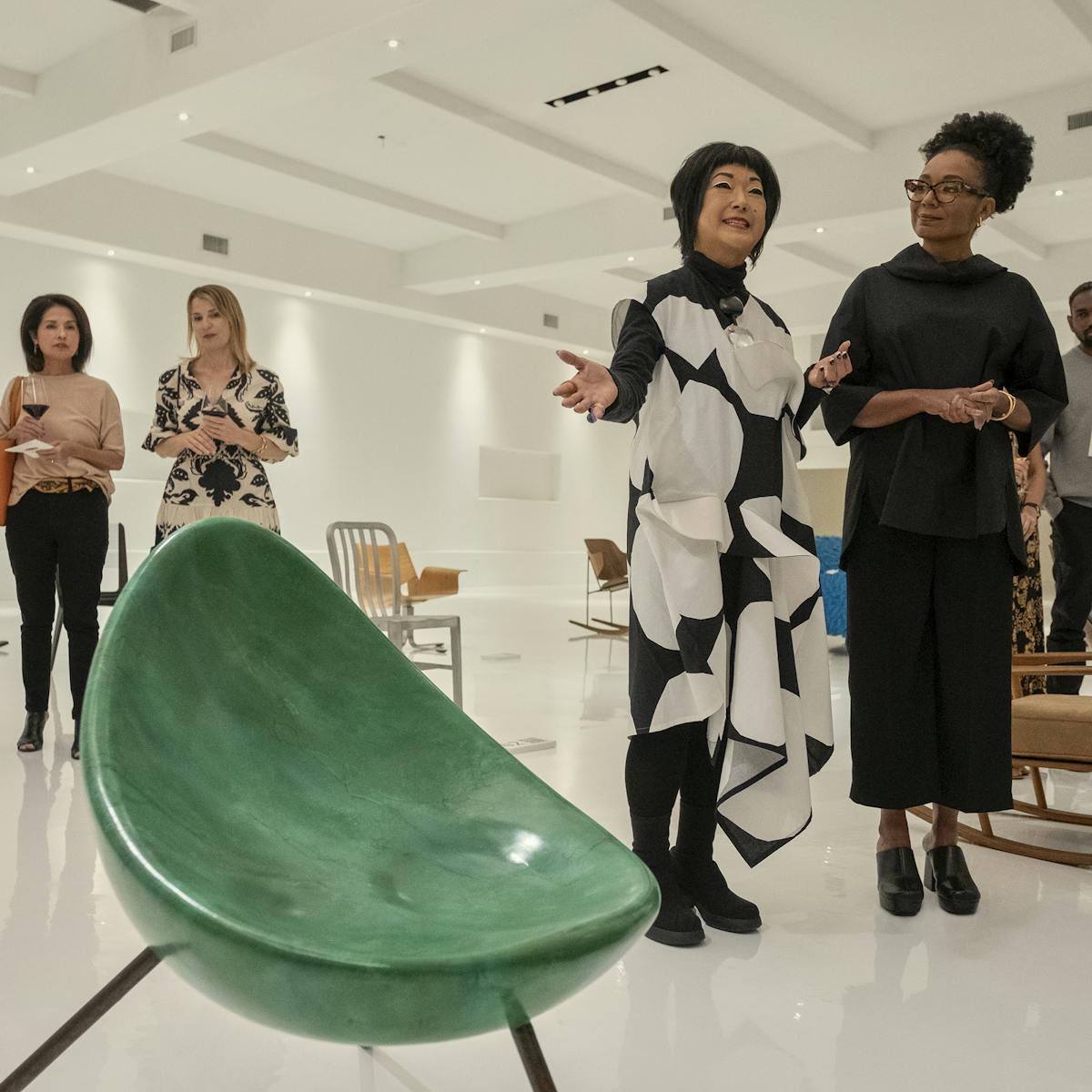 Fumi (Patti Yasutake) talks to a crowd of people about the green Tamago chair, which sits threateningly in the foreground of this shot.  
