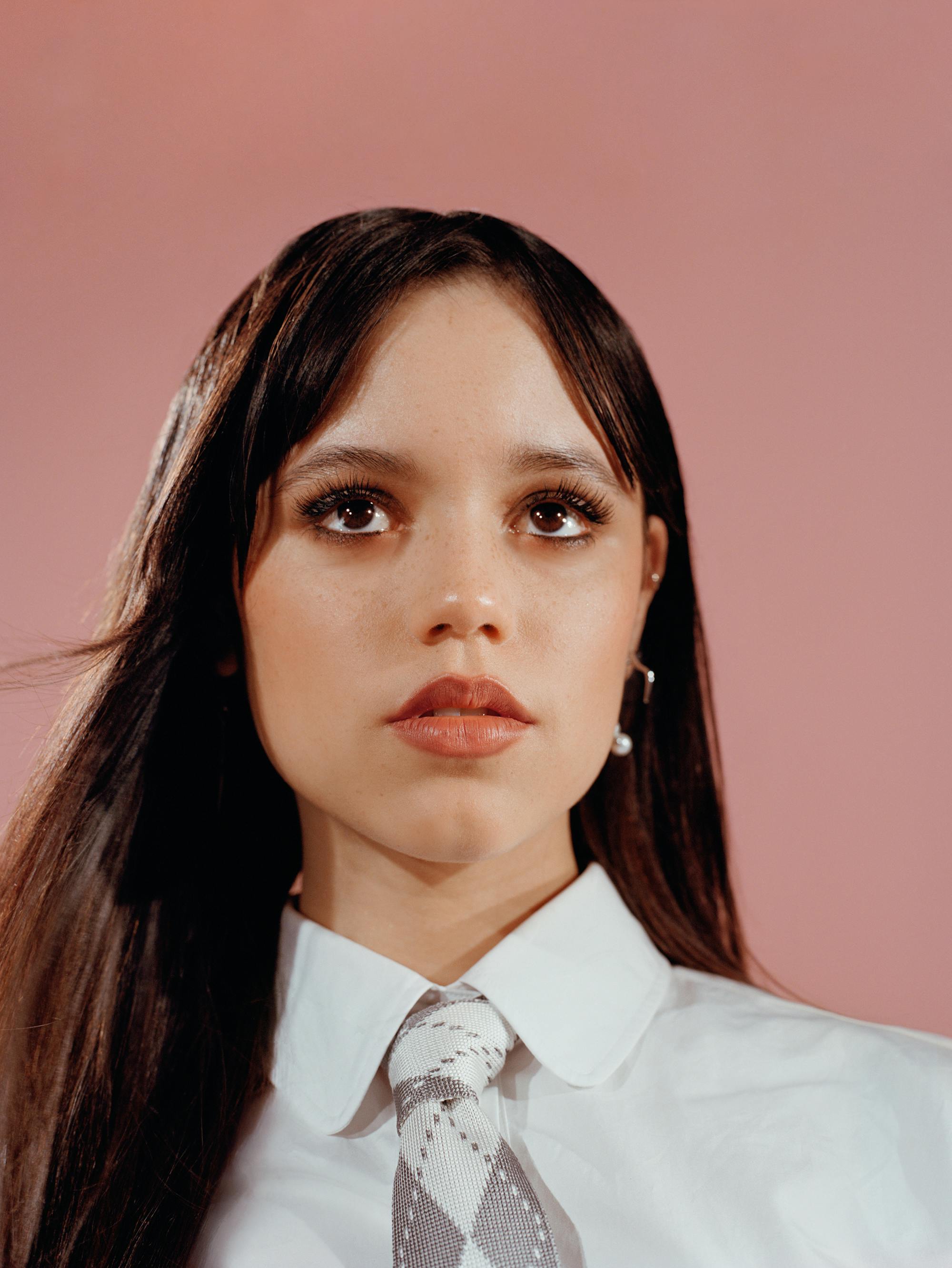 Jenna Ortega wears a white button-down shirt and an argyle tie. 