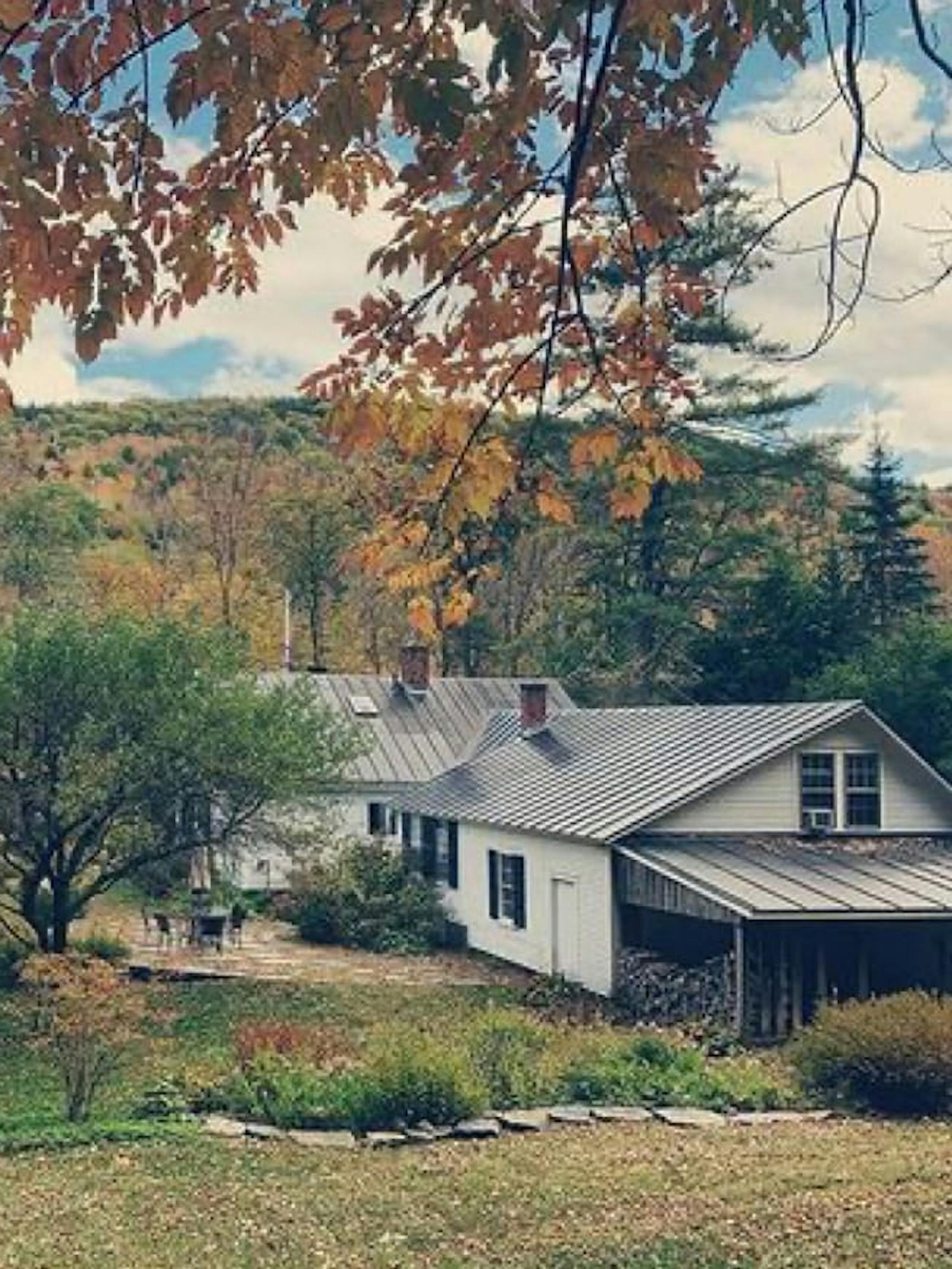 This is a picture of the Grafton House in a lovely fall scene. The house is white, with black shutters, and the foliage is red, orange, green, and yellow.