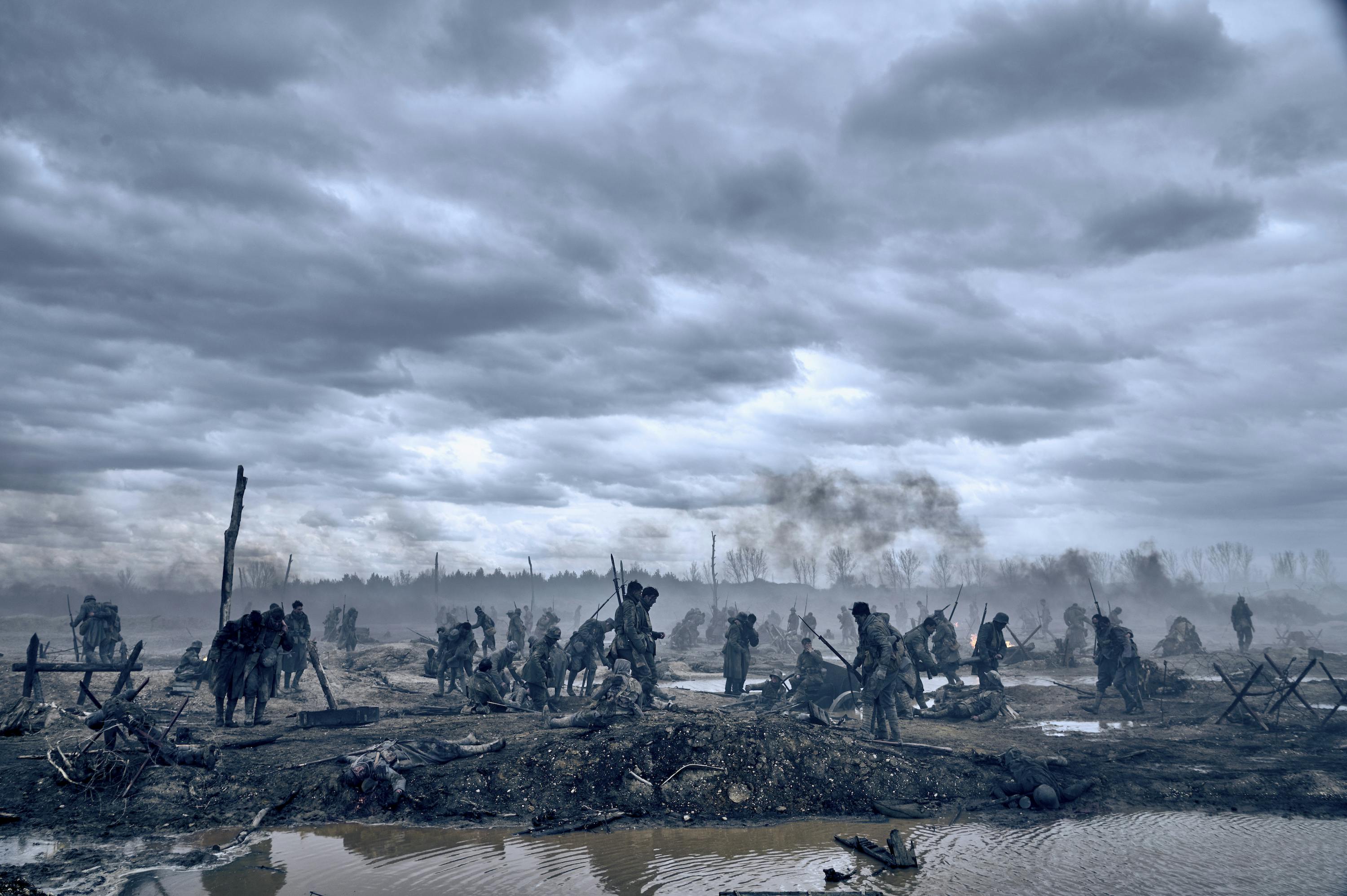 A barren scene from All Quiet on the Western Front features many soldiers walking through a muddy scene. 