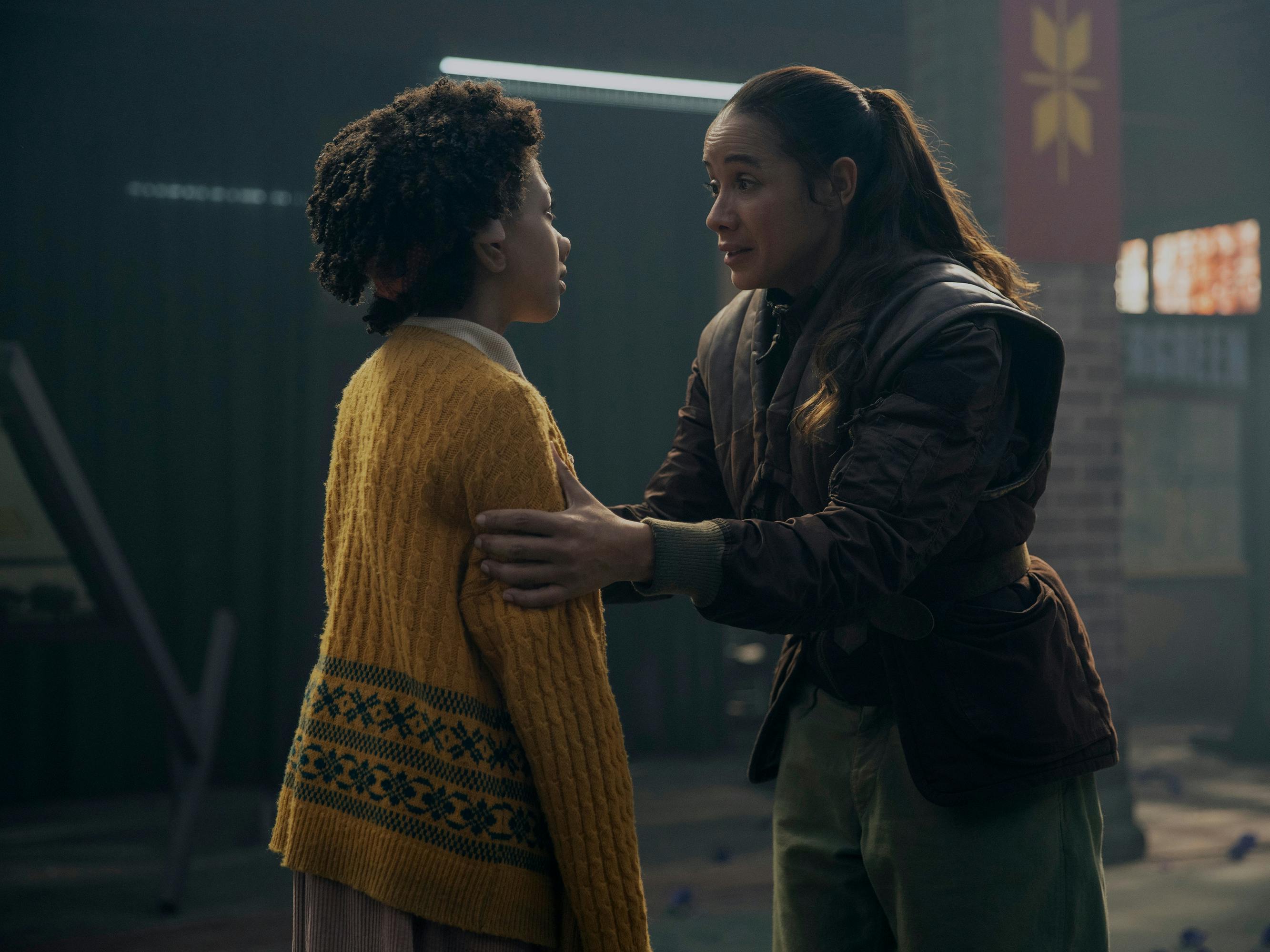 Wendy (Naledi Murray) wears a yellow sweater with her back to the camera. Aimee (Dania Ramirez) holds her by the arms with an insistent expression.