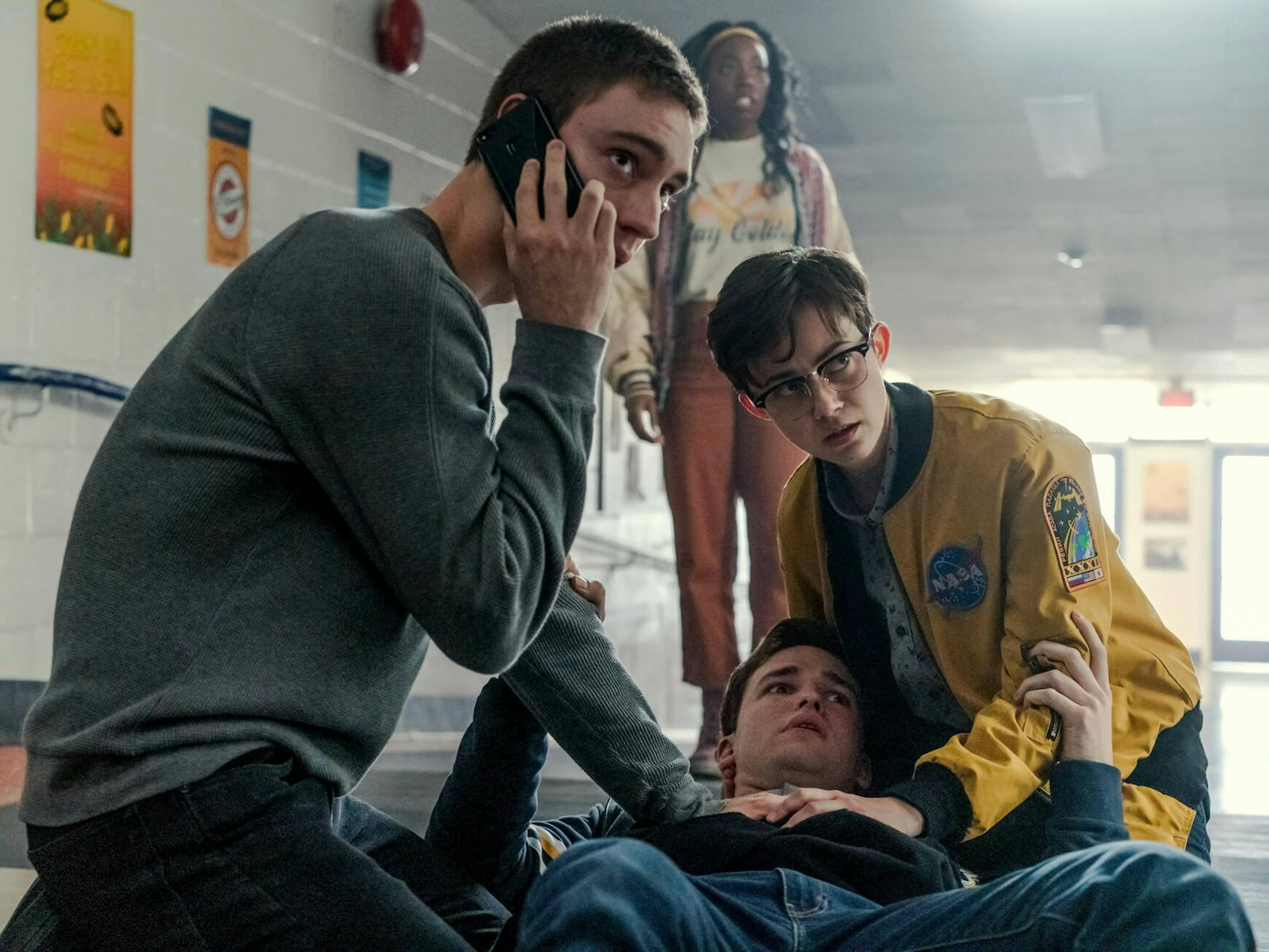 Ollie Larsson (Théodore Pellerin), Alex Crisp (Asjha Cooper), Caleb Greeley (Burkely Duffield), and Darby (Jesse Latourette) stand in a deserted halfway. Caleb lies on the ground as Ollie and Darby tend to him, while Alex stands behind them. Ollie makes a call with an urgent expression on his face.