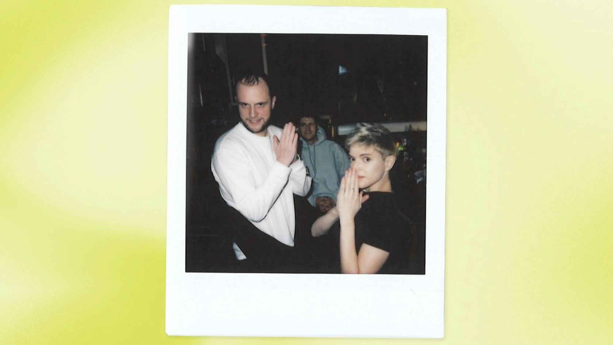 Mae with Jack Berry and friend in this polaroid shot. Mae wears a black t-shirt and Jack Berry wears a long-sleeved white shirt.
