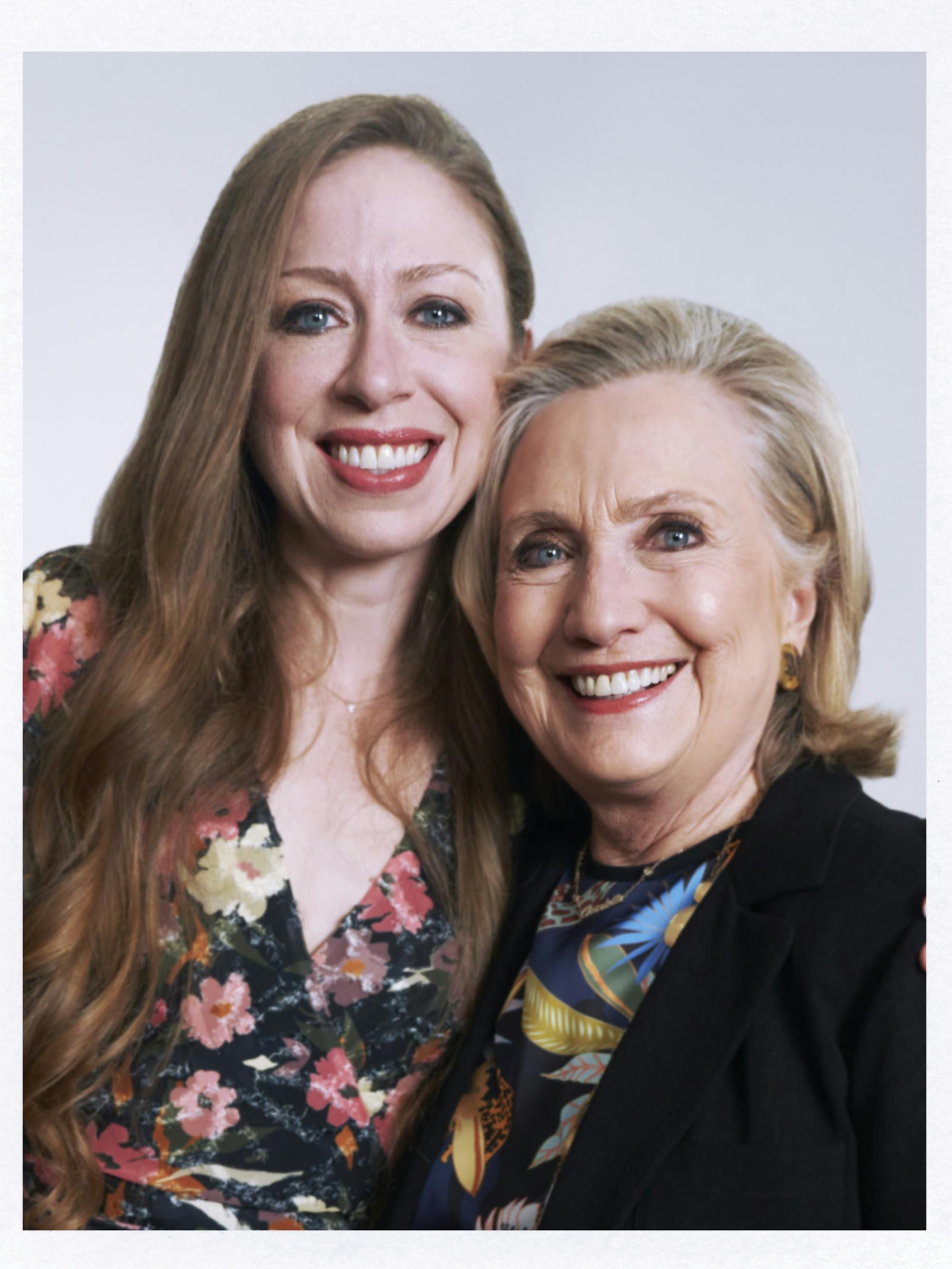 Chelsea and Hillary Clinton sit together against a white background. Chelsea wears a floral top and Hillary wears a patterned shirt underneath a black blazer.