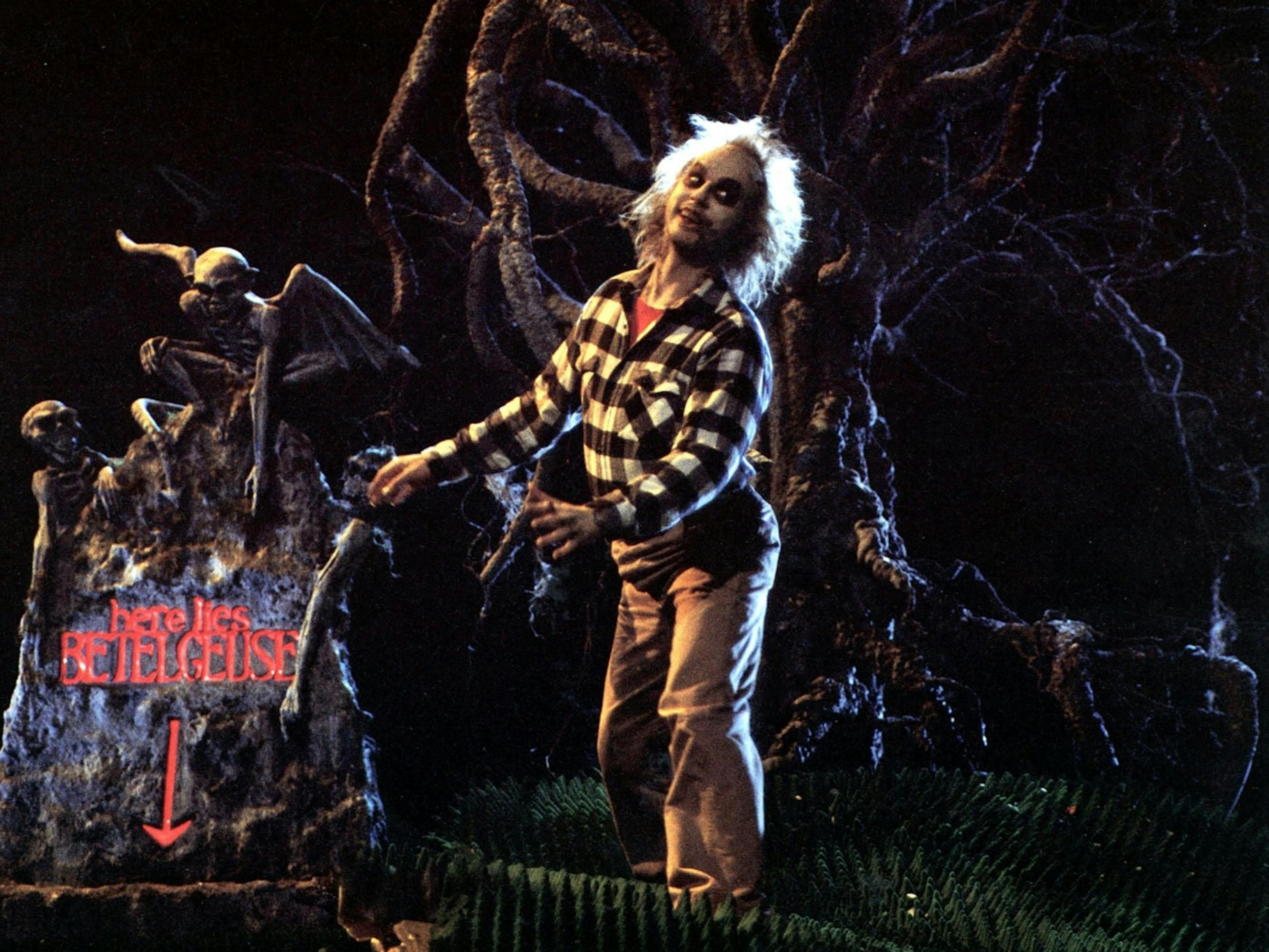 Betelgeuse (Michael Keaton) in Beetlejuice stumbles through gnarled roots, past a grave marked “here lies Betelgeuse.